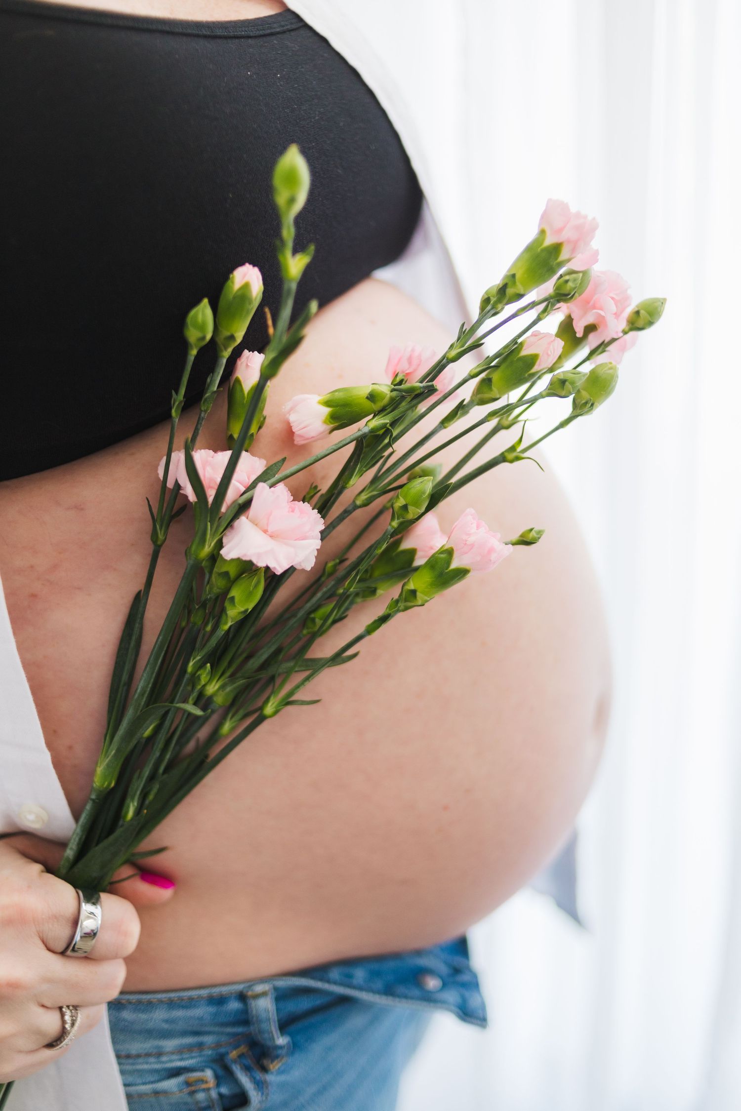 A close-up shot of a pregnant belly with delicate pink carnations against black clothing.
