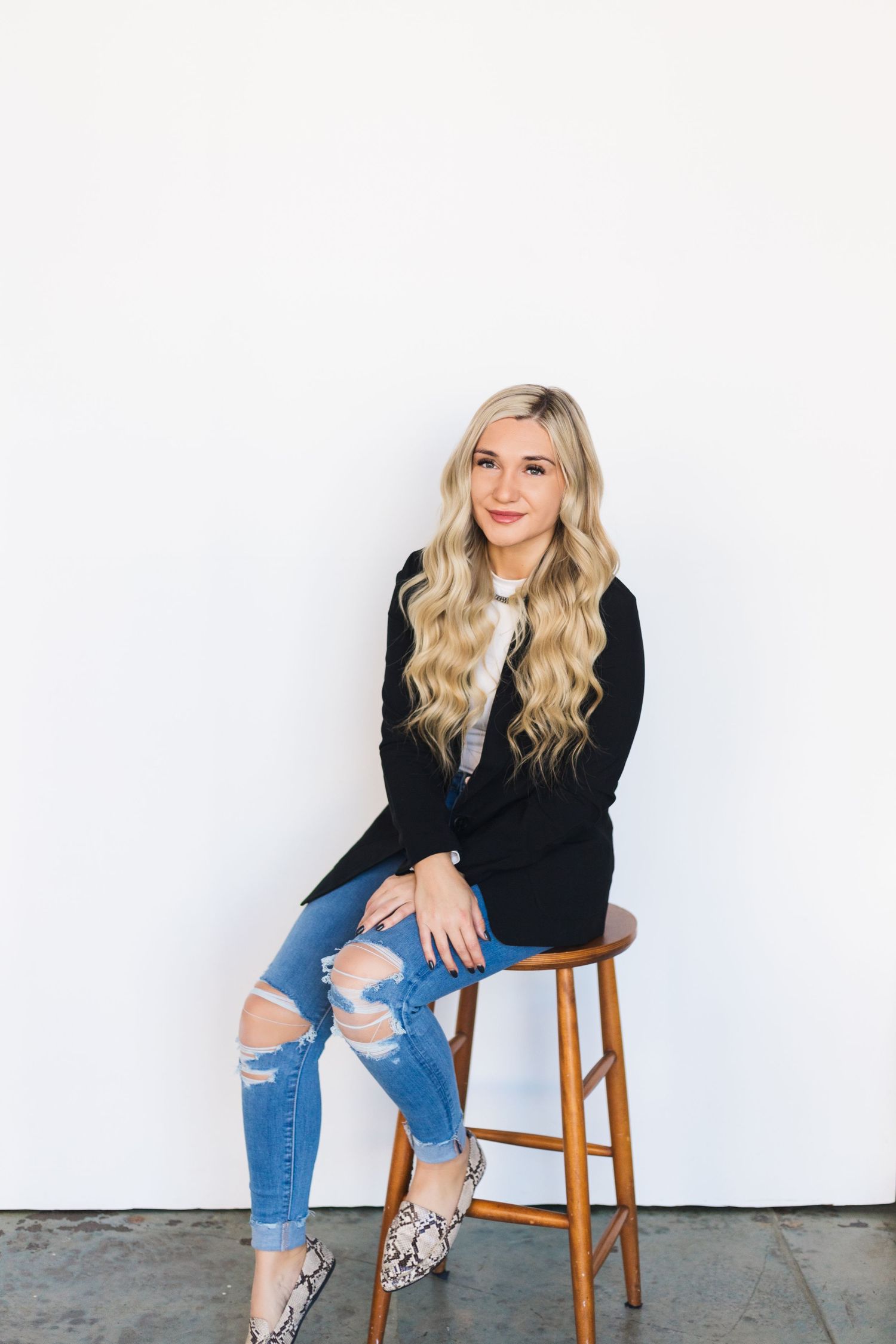 Casual portrait against white wall wearing black cardigan, ripped jeans and snakeskin flats.