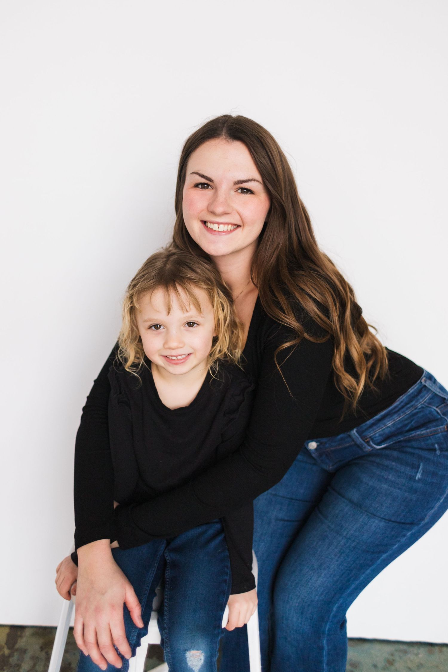 Family portrait of two people wearing matching black tops and jeans against white background.