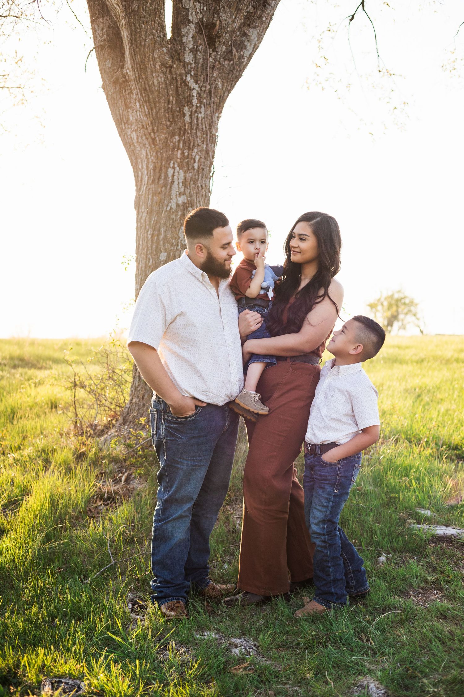 A family poses together under a large tree in a sunlit field during golden hour.