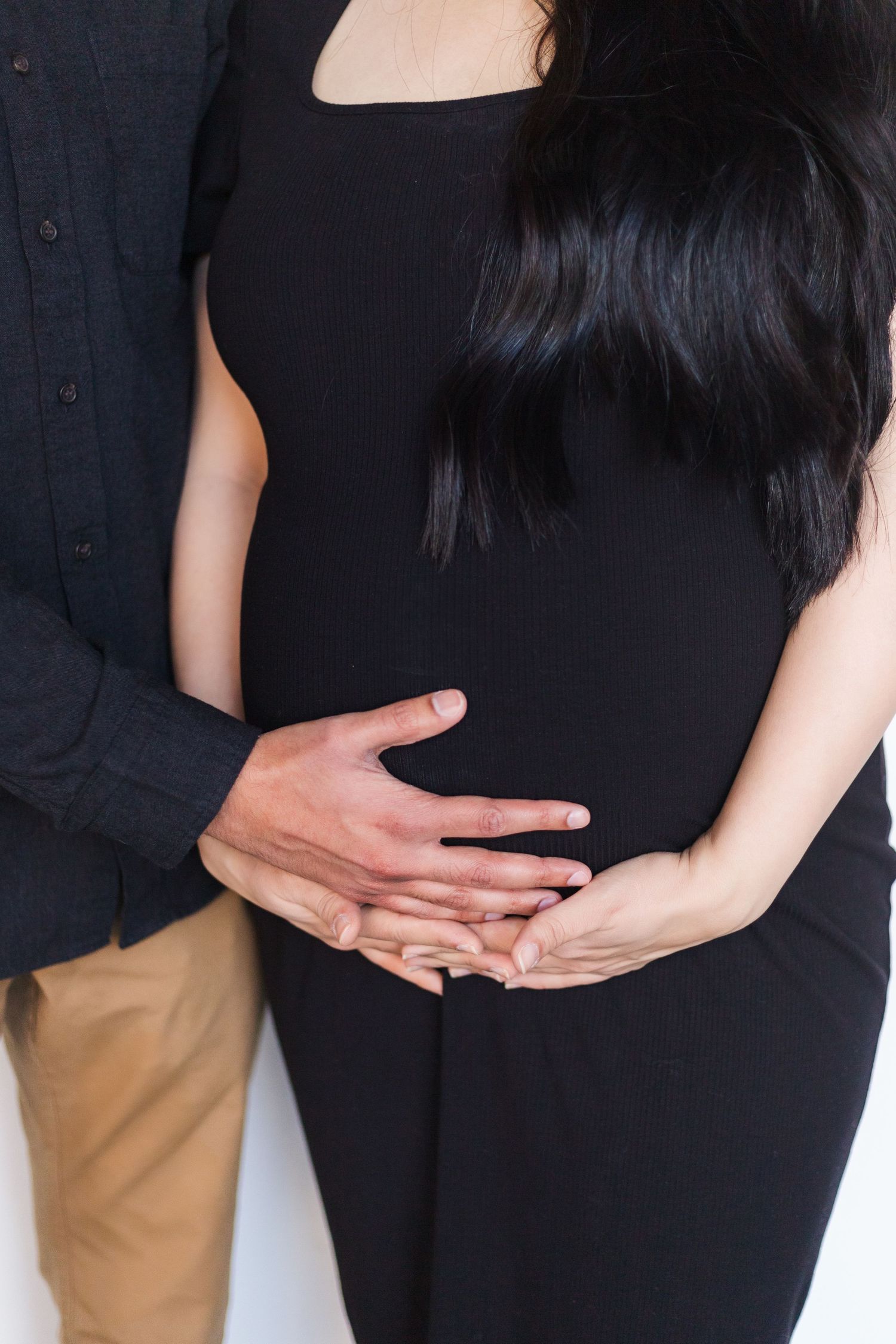 Close up of couple's hands cradling together against white backdrop.
