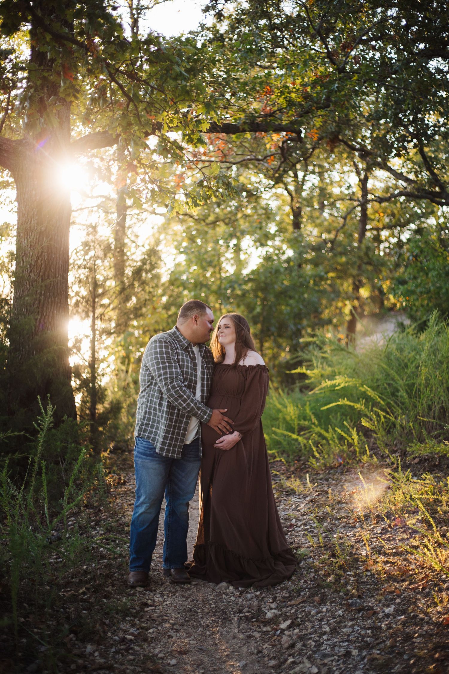 Romantic outdoor photo session in golden sunlight with couple embracing against large tree trunk in autumn setting.