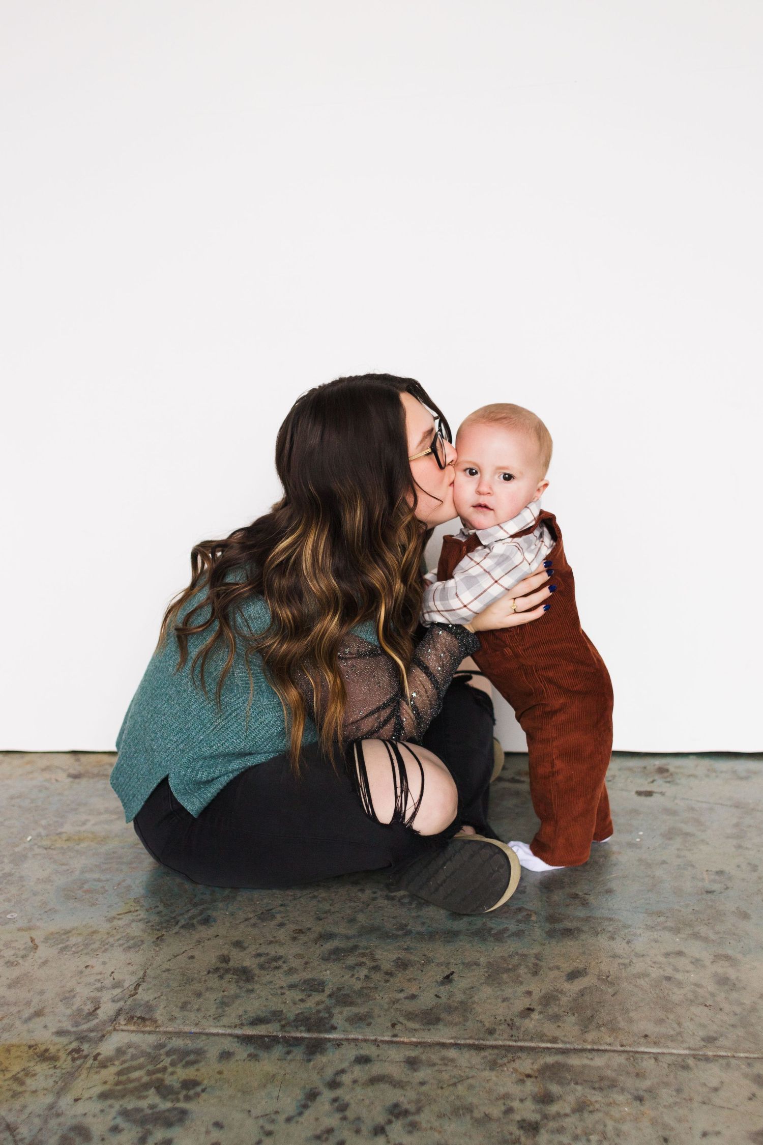 An intimate portrait of parent and baby sharing affectionate moment on concrete floor.