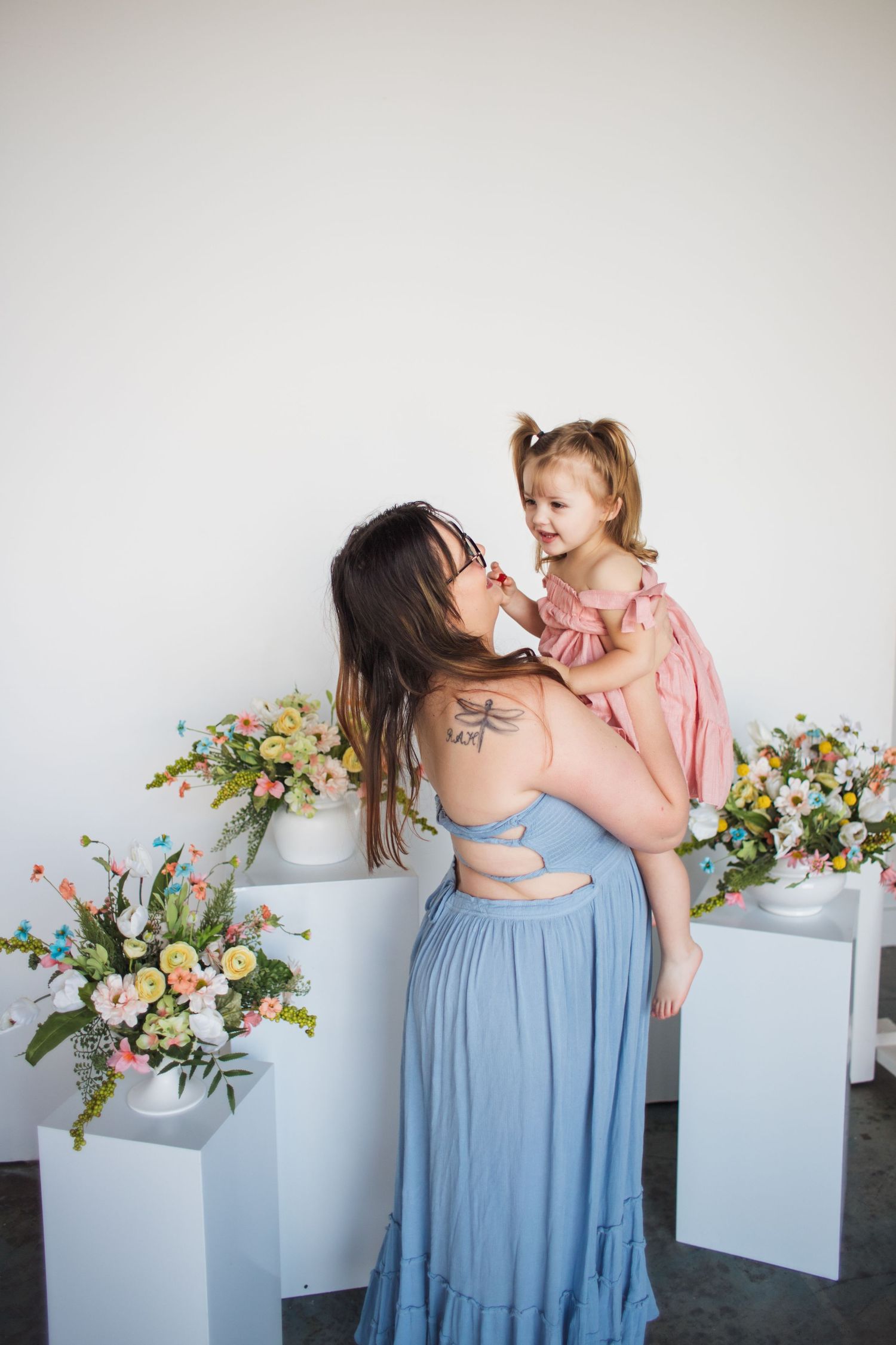 Two flowing dresses in blue and pink tones photographed with floral arrangements in studio setting.