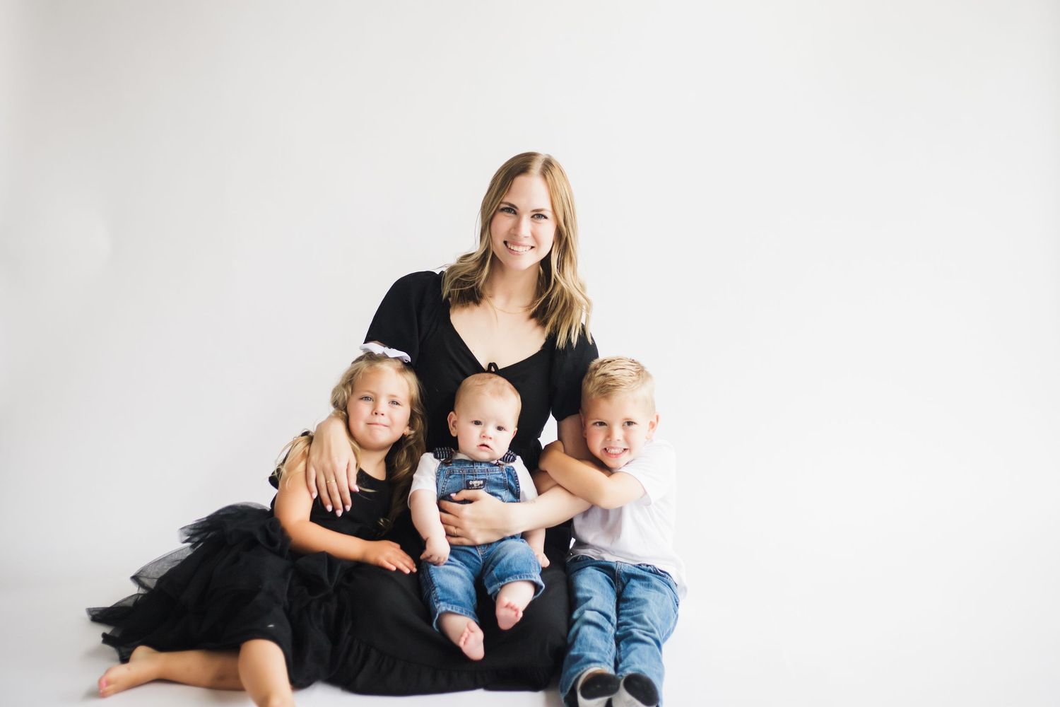 A family in coordinating black and white outfits poses together on a light backdrop for professional portraits.