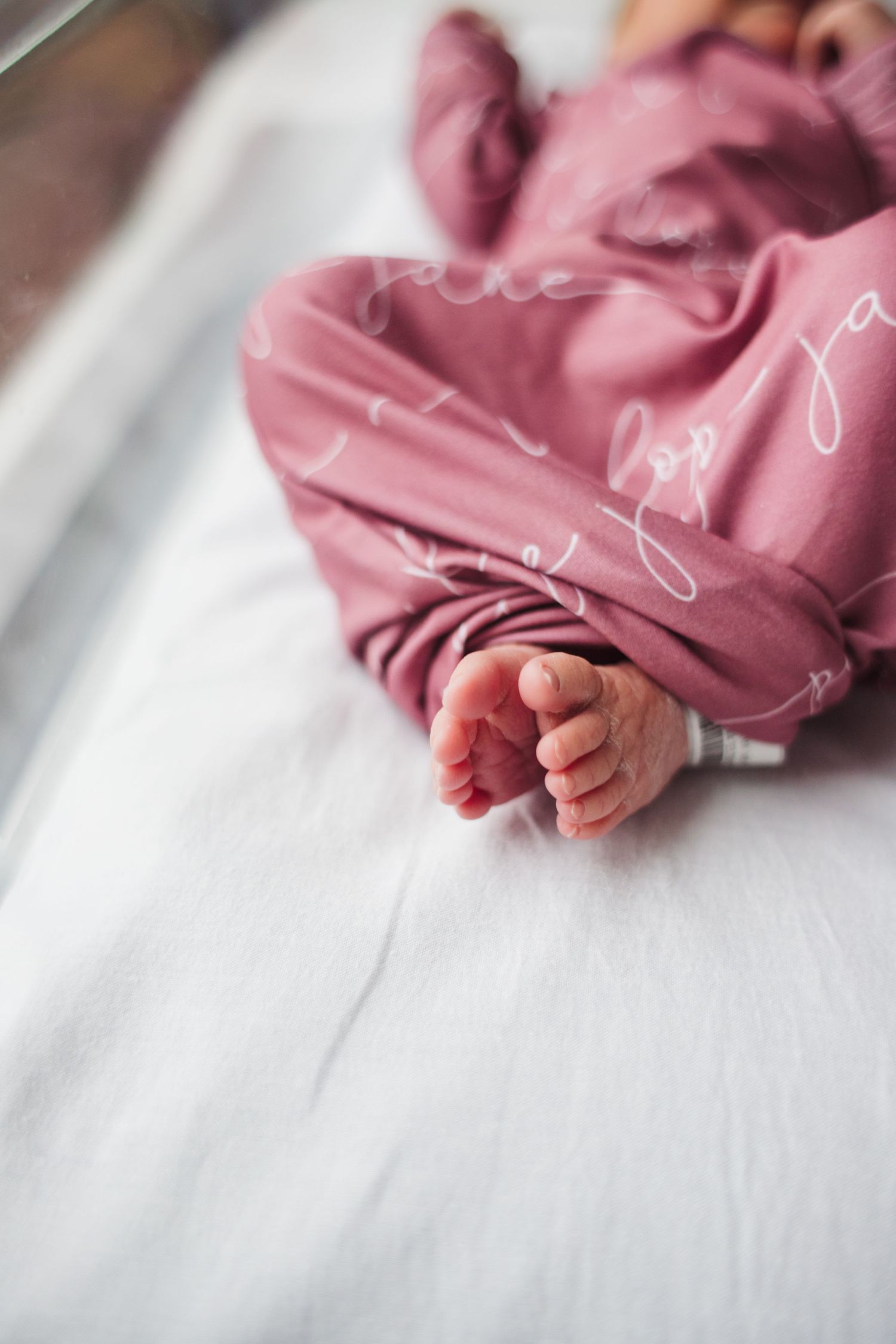 Close up view of tiny baby feet wrapped in soft pink swaddle blanket on white surface.