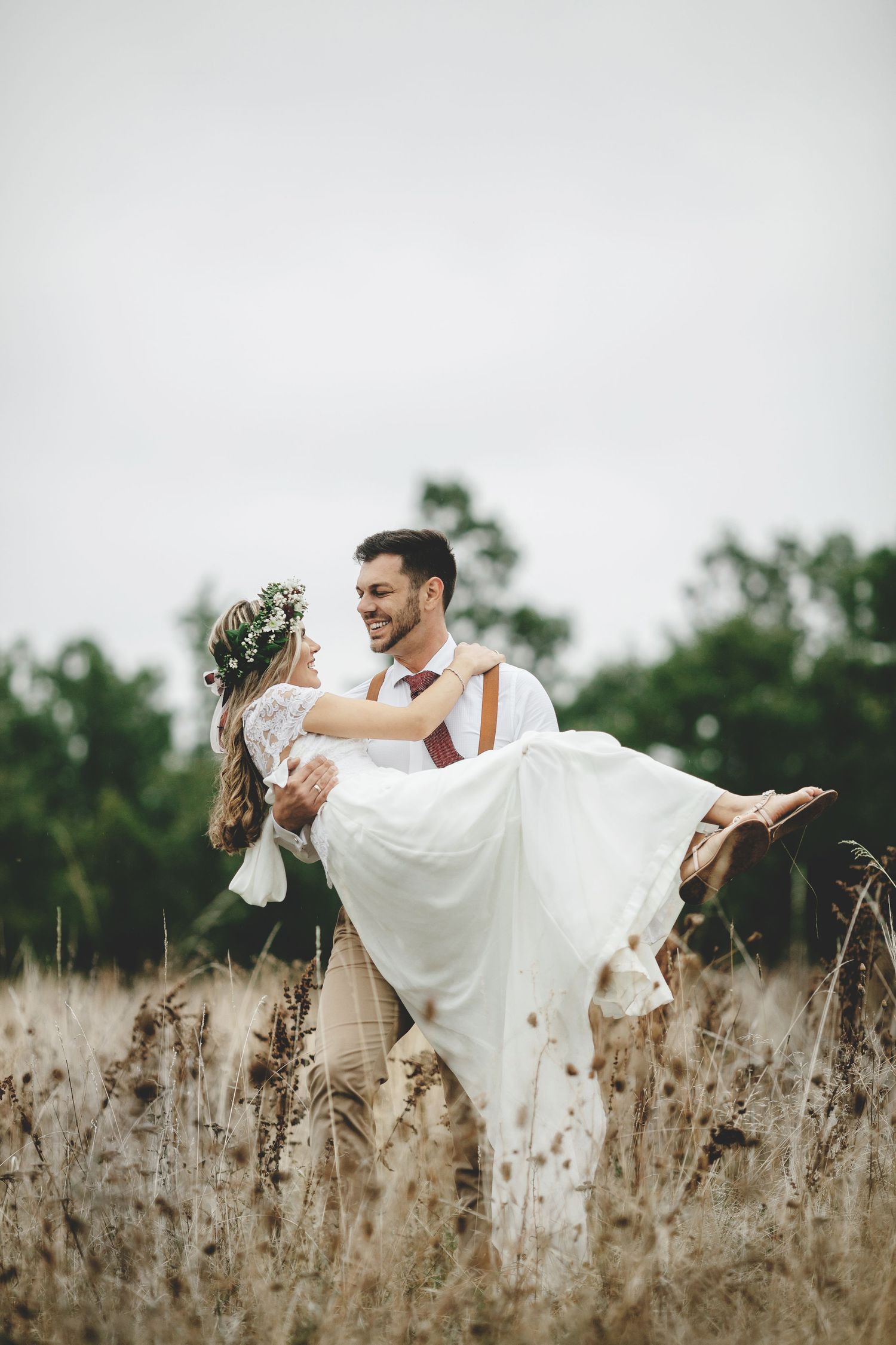 Romantic wedding portrait with groom carrying bride through a field of tall grass.