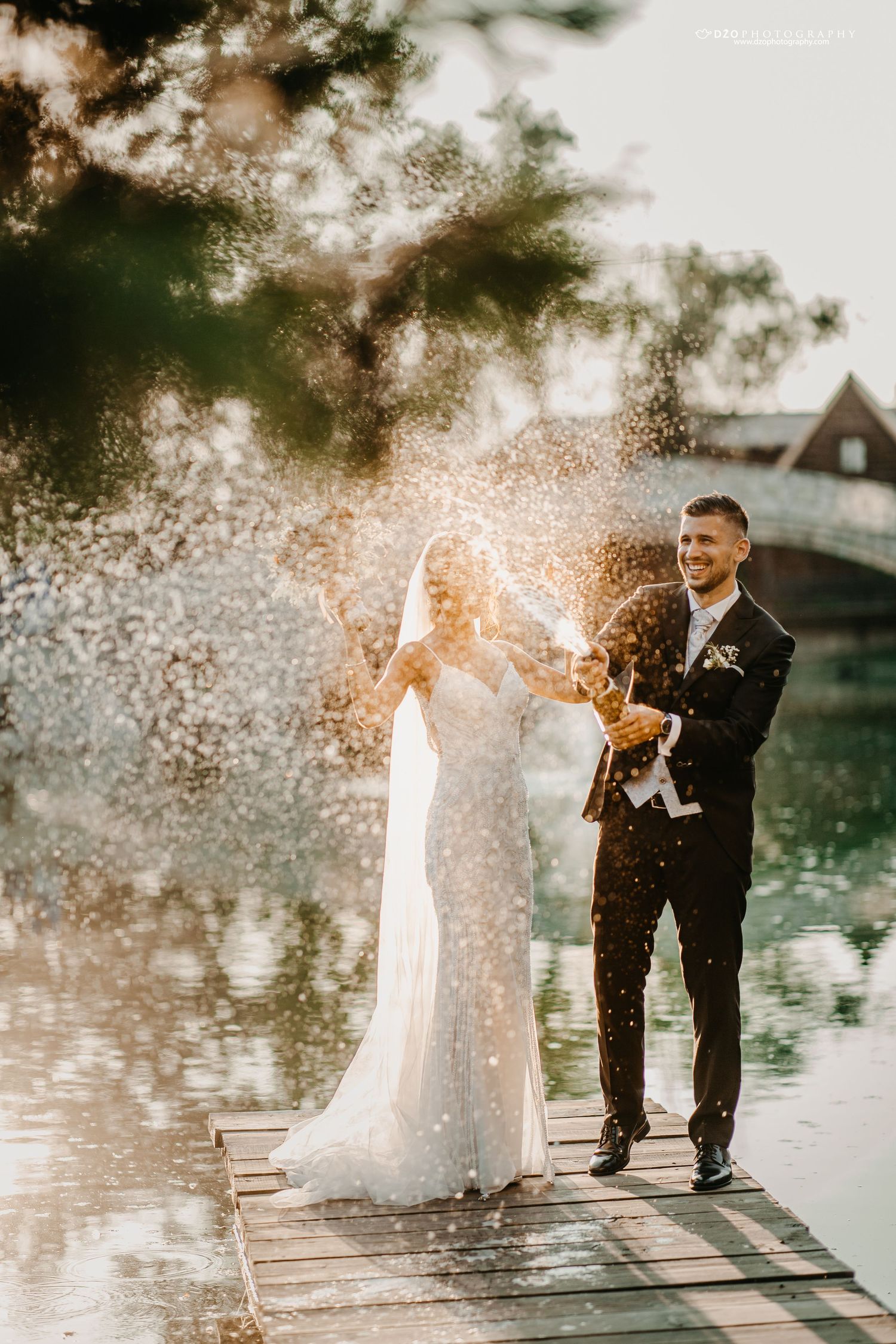 Couple spraying champagne on a dock during golden hour celebrations.