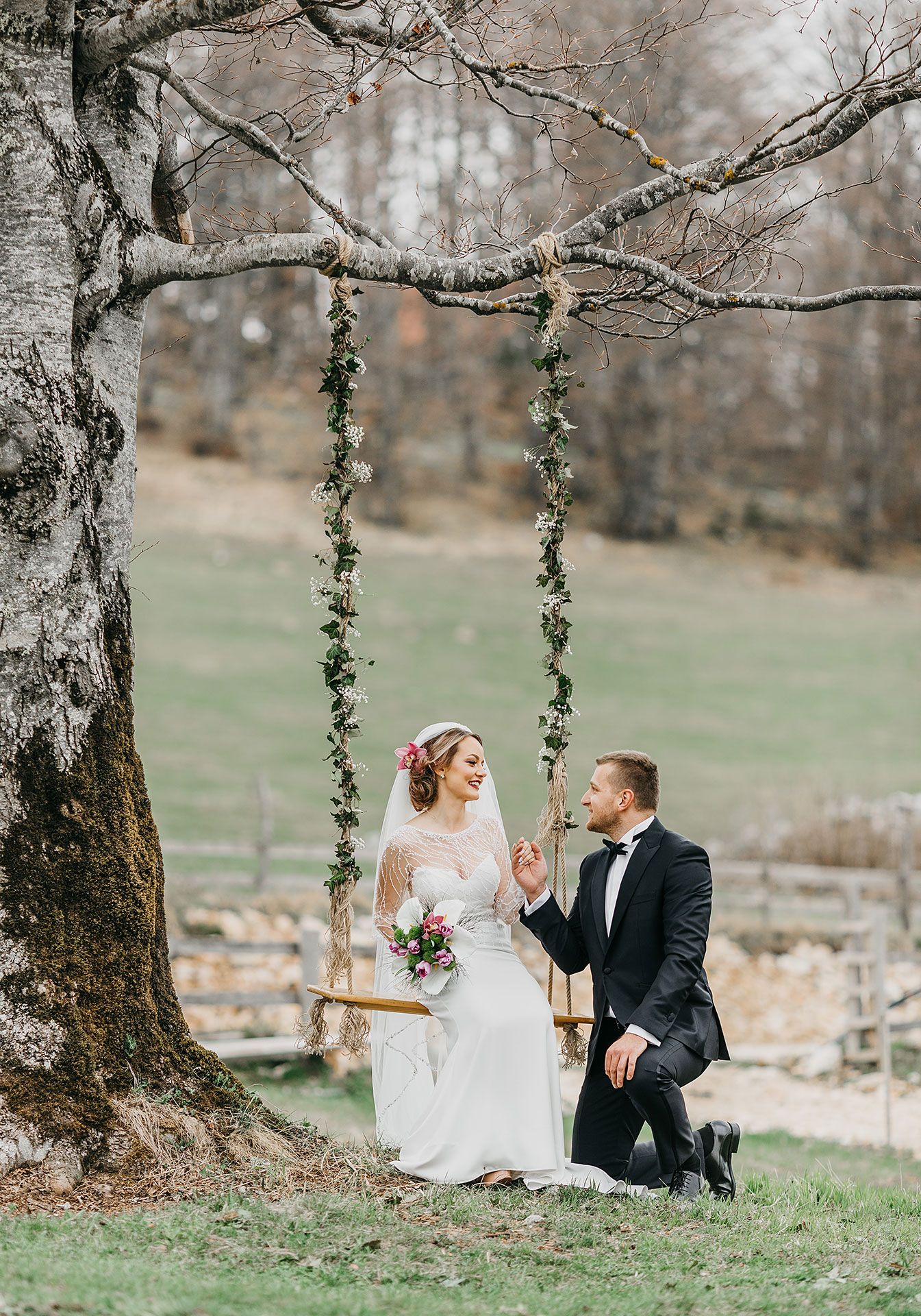Romantic wedding photo of a couple on a rustic tree swing decorated with greenery garlands.