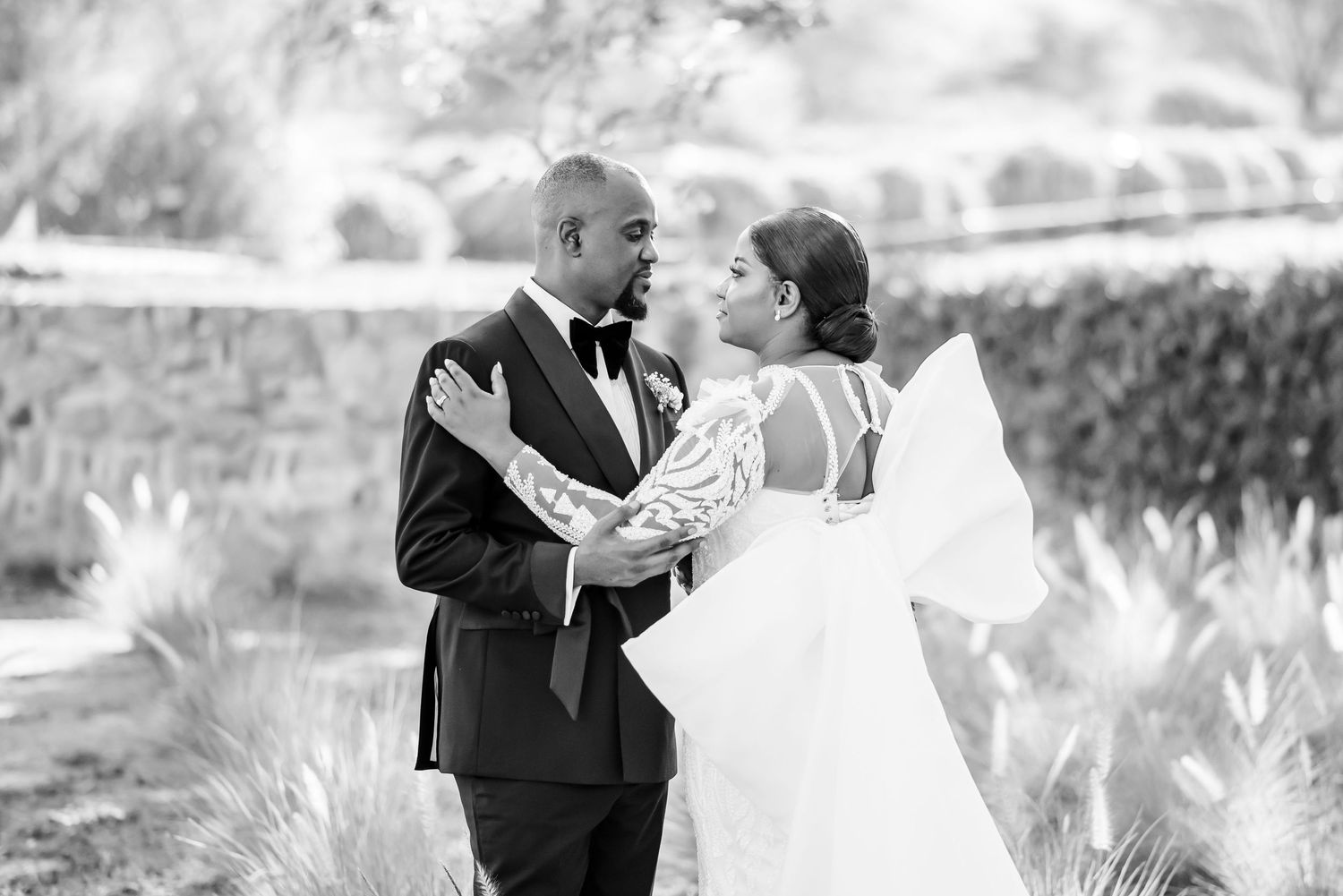 A romantic black and white wedding photo of a happy couple embracing outdoors with a flowing white gown.