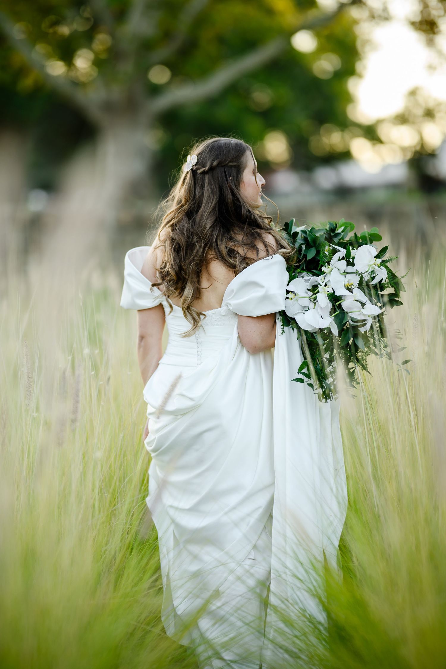 A figure in a flowing white dress twirls gracefully through a sunlit meadow of tall grass and wildflowers.