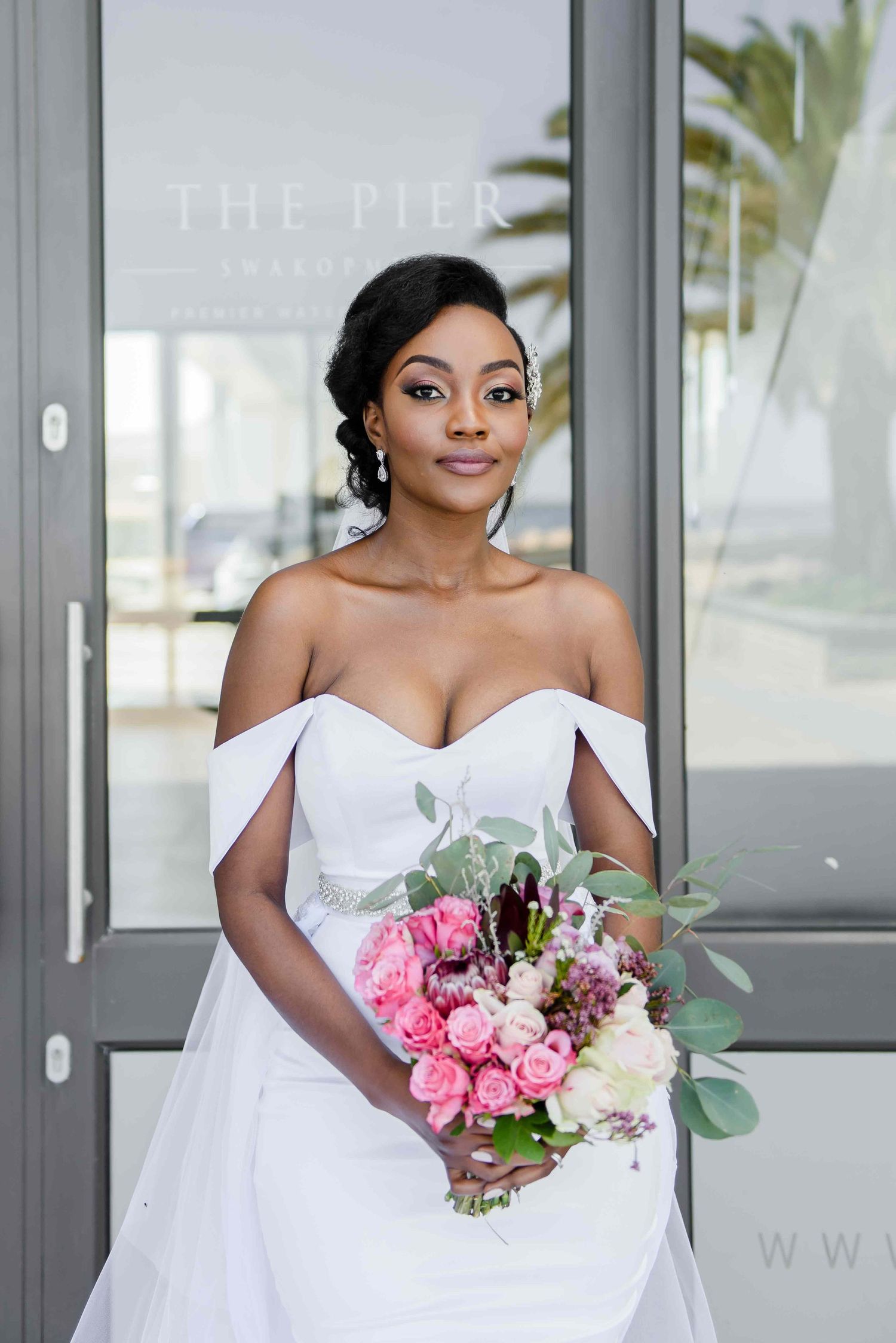 Elegant bride in off-shoulder white gown holding pink and white bouquet in Swakopmund.
