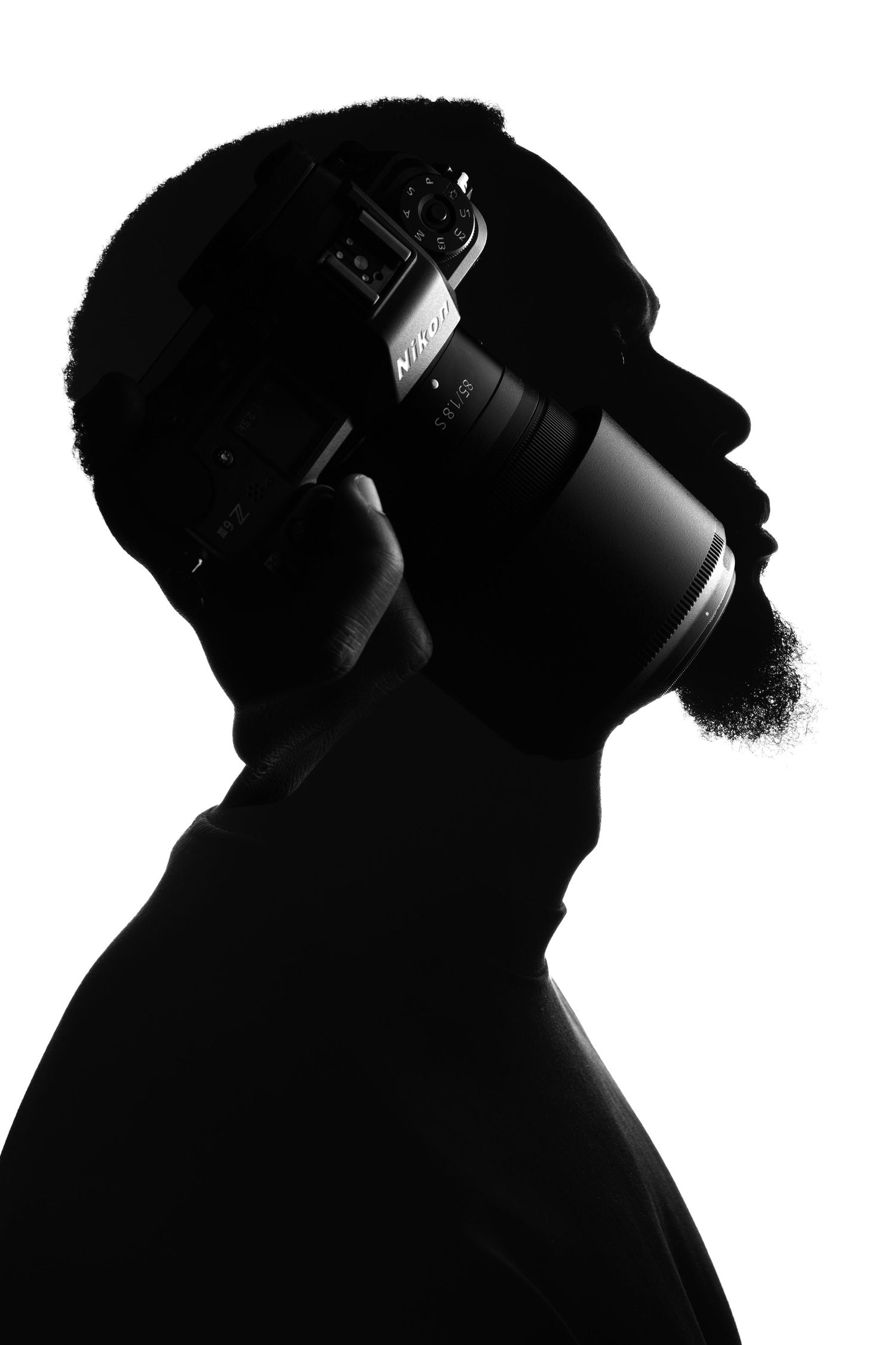 Black and white silhouette profile of photographer holding camera against dark background.