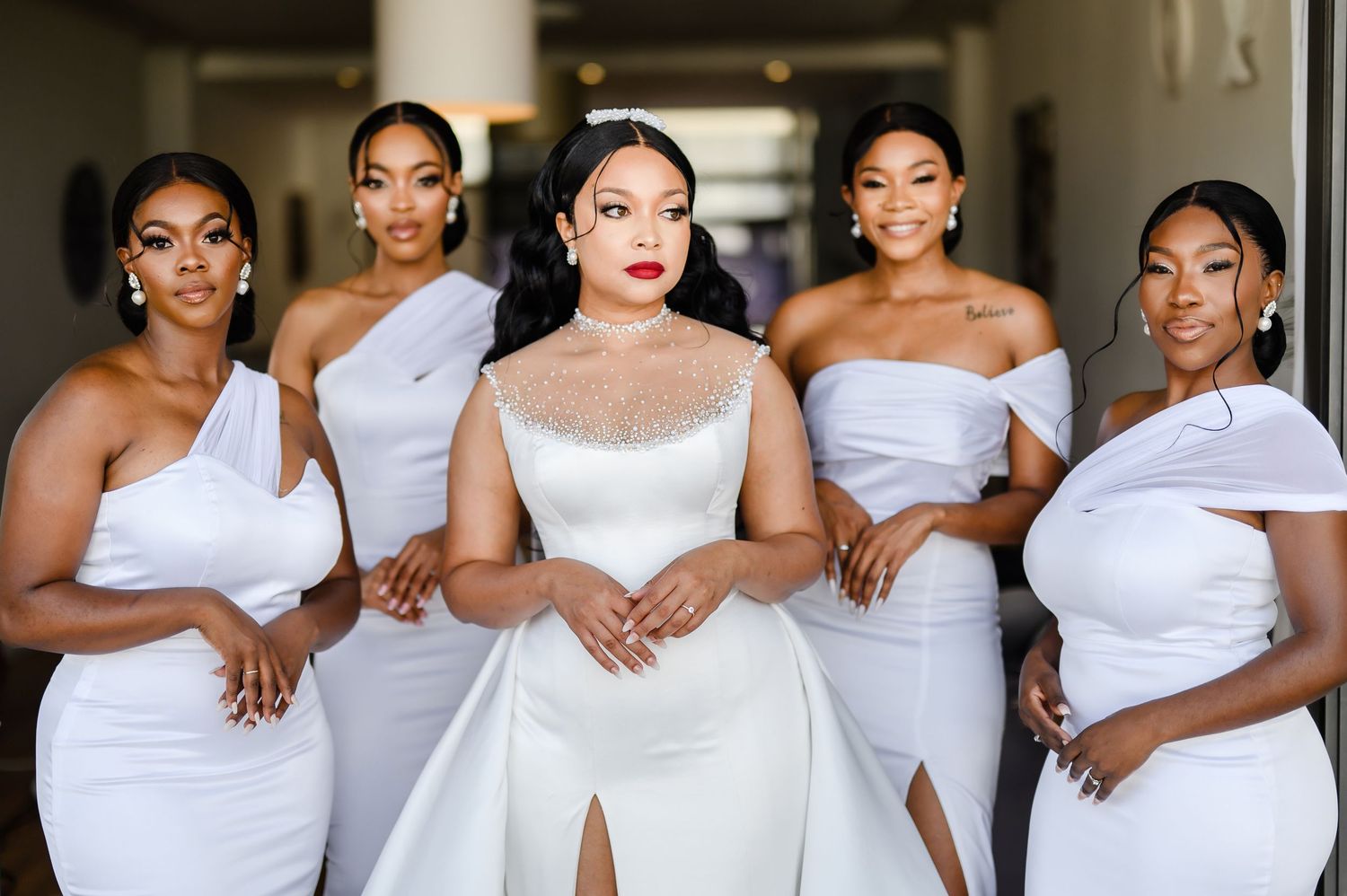 Wedding party photo of bride in white dress surrounded by four bridesmaids in elegant white gowns.
