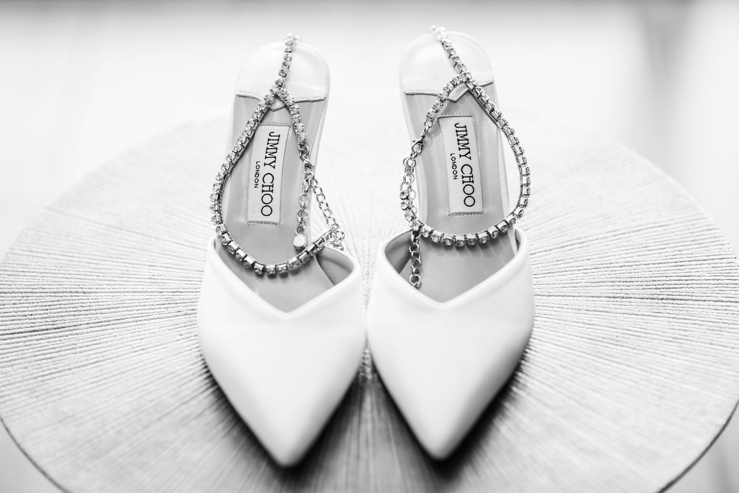 Elegant white bridal shoes with crystal straps photographed in black and white.