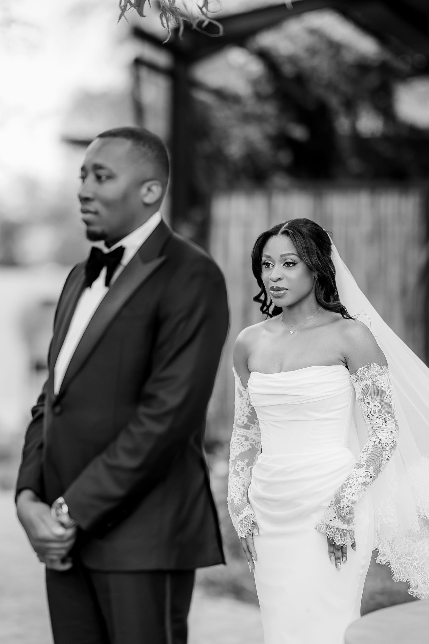 A romantic black and white wedding portrait shows the bride in a lace-sleeved gown with veil looking over her shoulder.