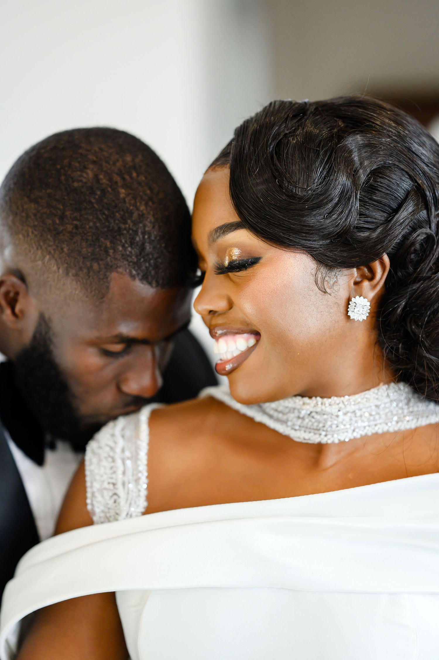 A loving couple shares an intimate moment in elegant wedding attire featuring white formal wear and stylish accessories.