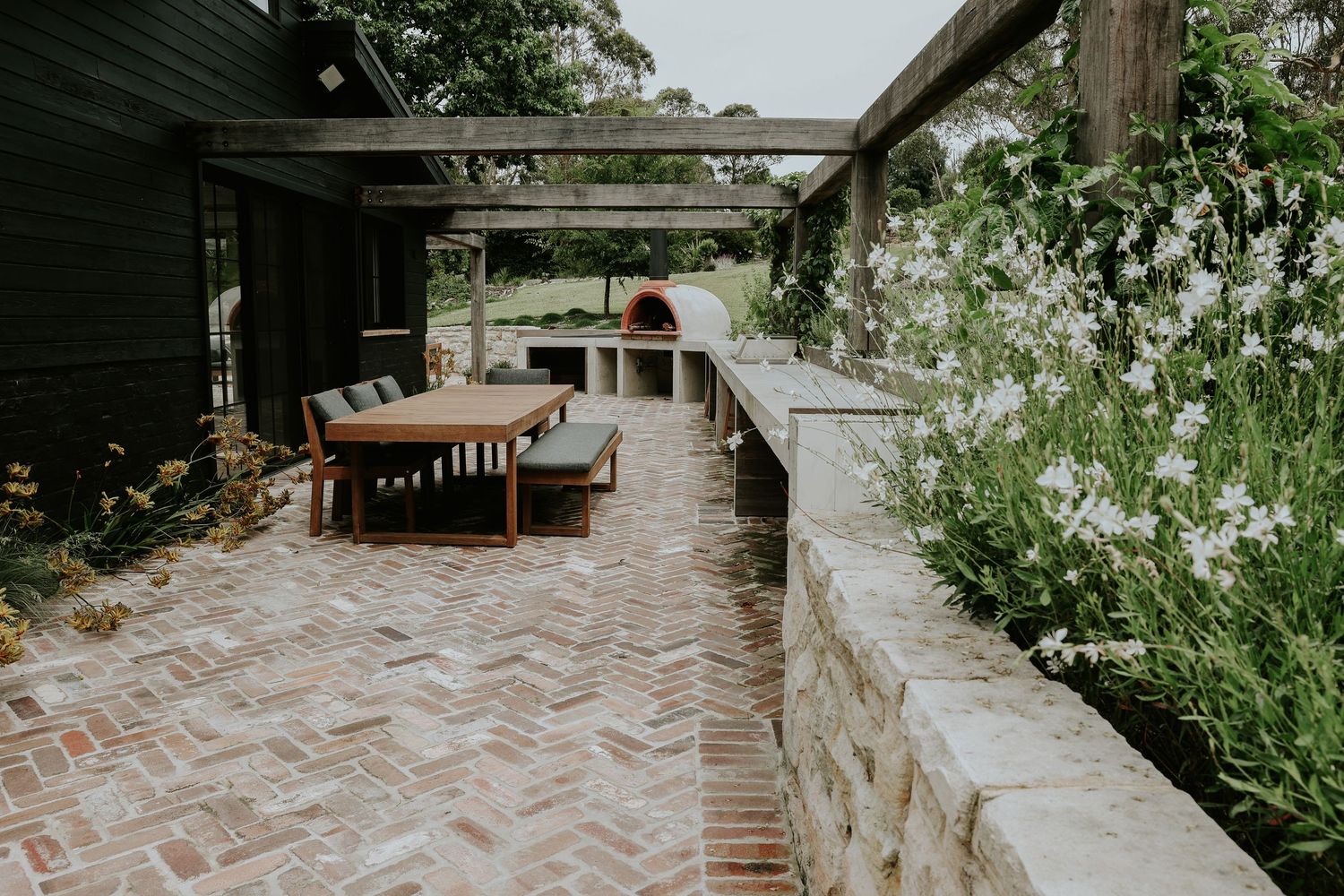 Outdoor dining area with brick patio, pergola, and pizza oven.