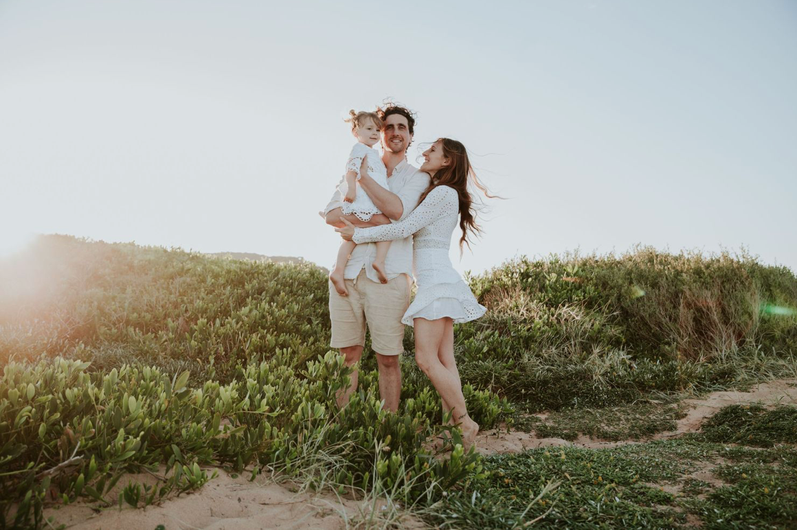 Happy young family with baby enjoying a sunny day on coastal sand dunes near the ocean.