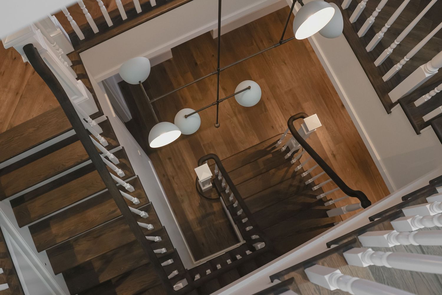 Aerial view of elegant wooden staircase with white globe pendant lights and dark hardwood floors.