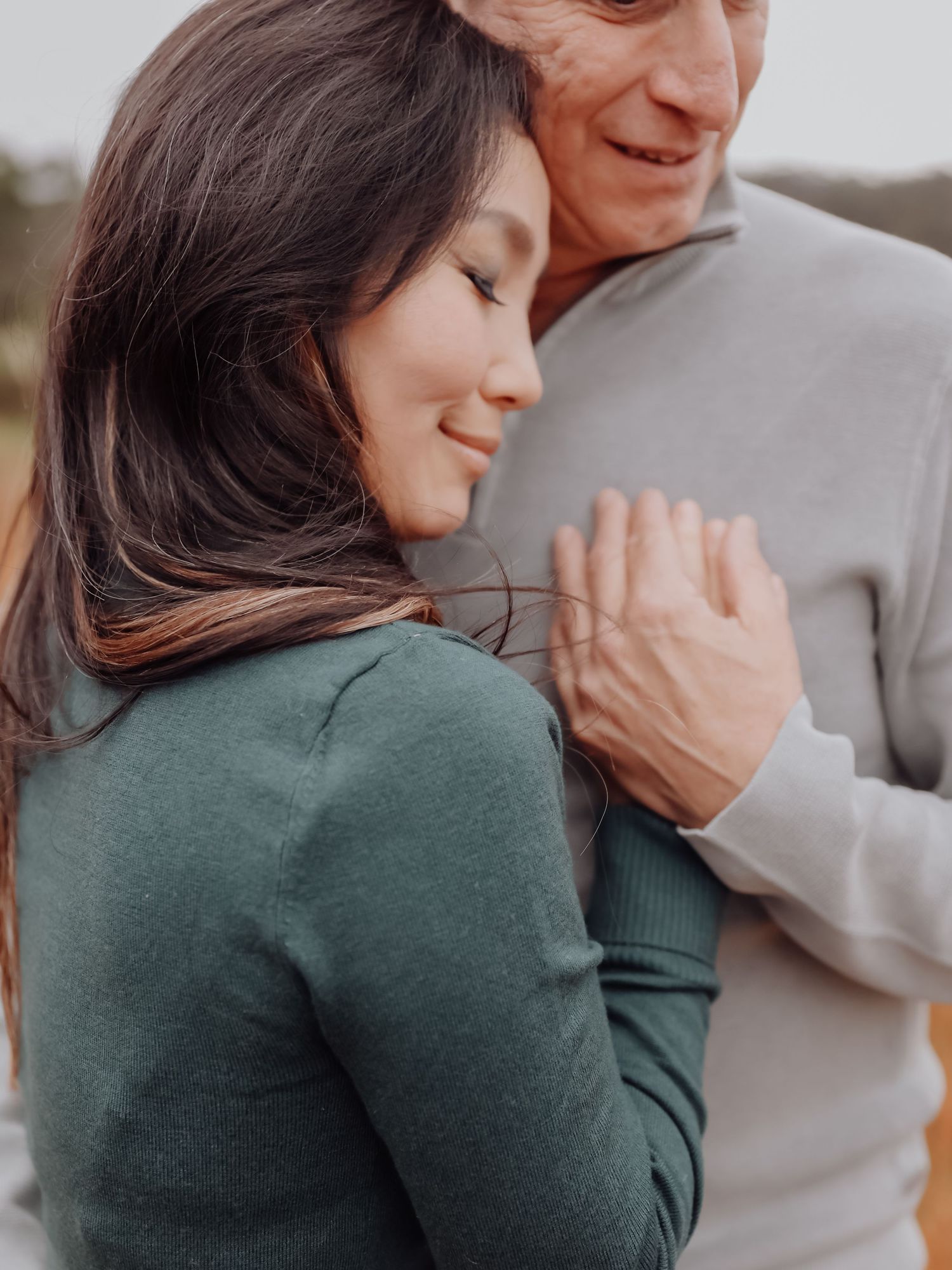 Couple sharing a tender embrace outdoors, woman smiling with eyes closed.