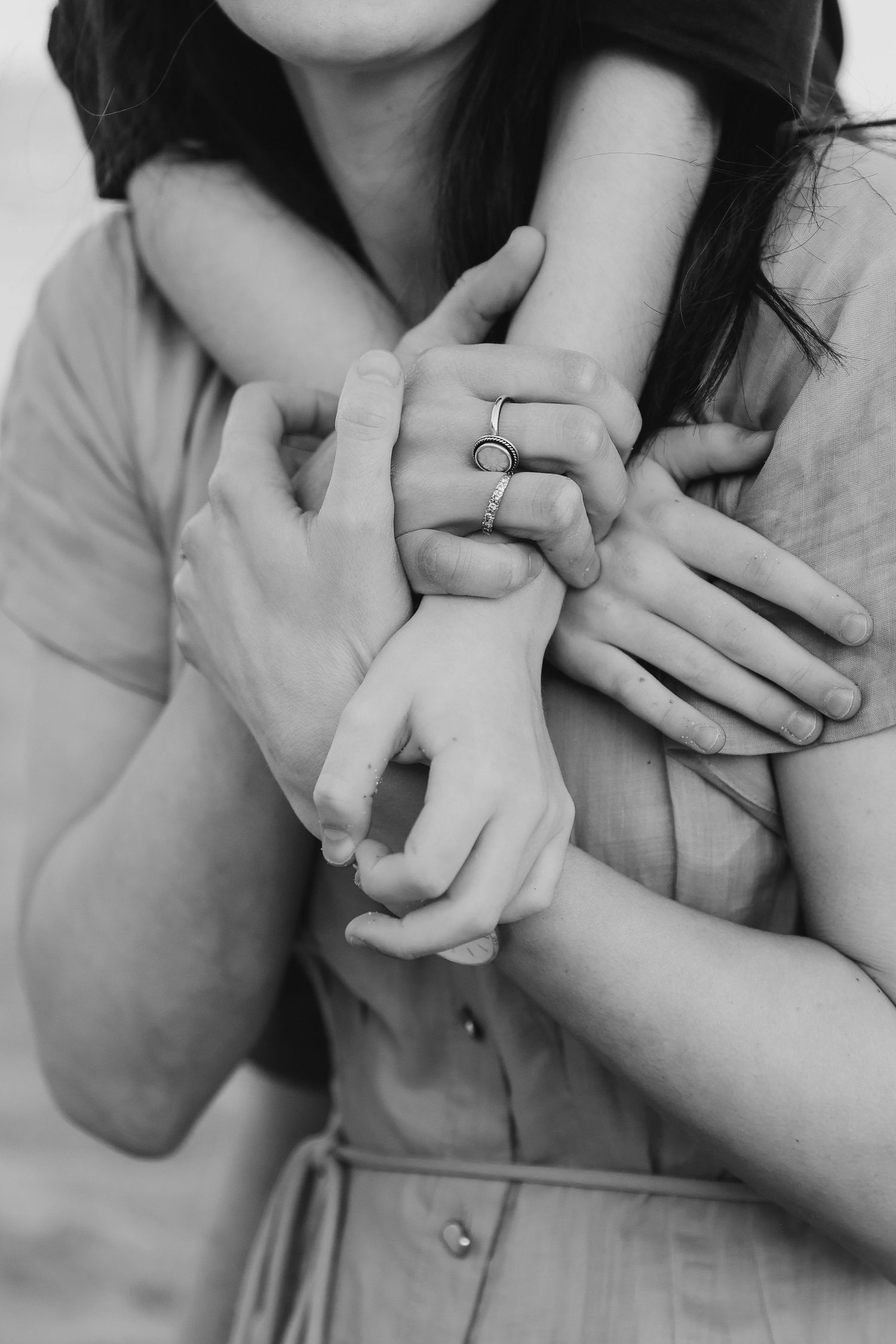 Black and white photo of a couple embracing, their hands intertwined, woman wearing a delicate ring.