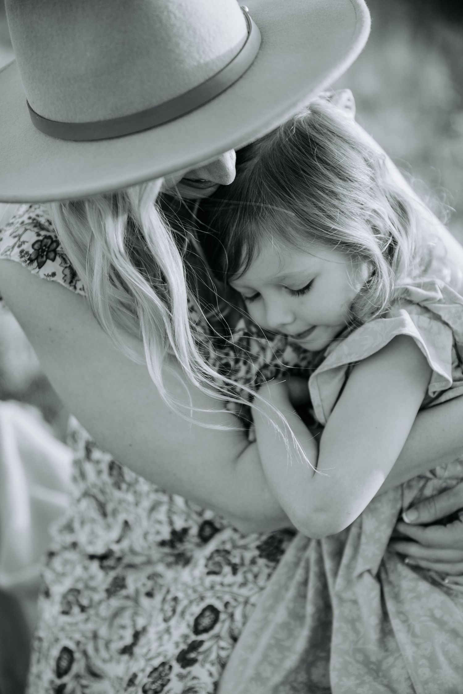 Black and white photo of mother in wide-brim hat hugging young daughter tenderly.