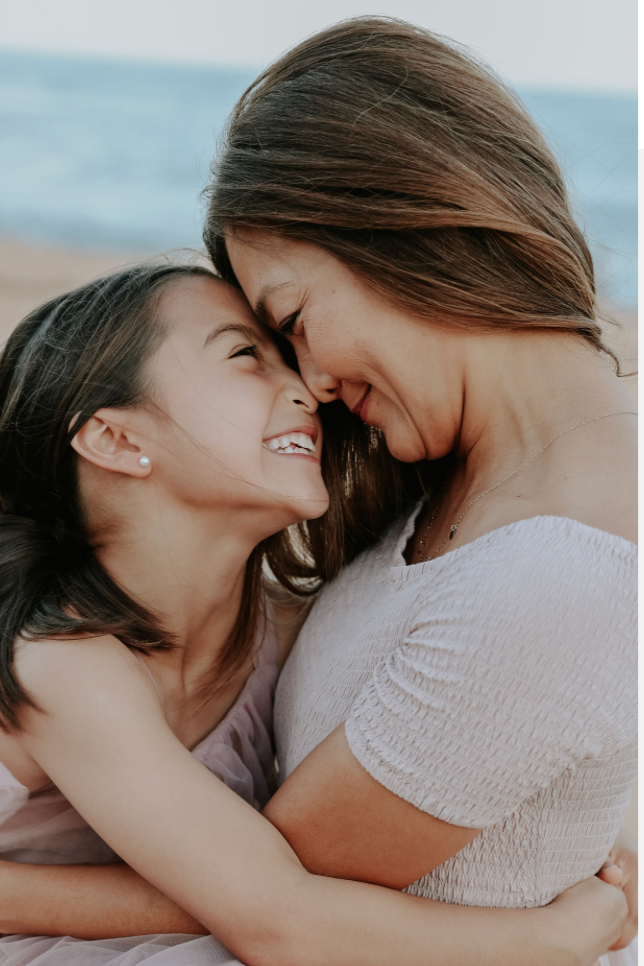 Mother and daughter sharing a joyful nose-to-nose moment on a beach, smiling warmly.