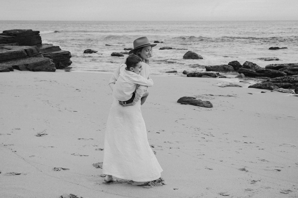 A black and white image of a woman in a white dress holding a child on the beach.