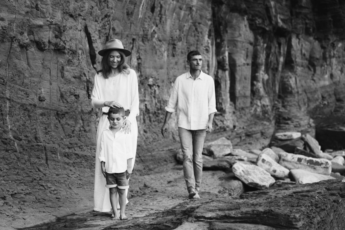 A black and white photo of a family of three standing near rocky coastal cliffs.