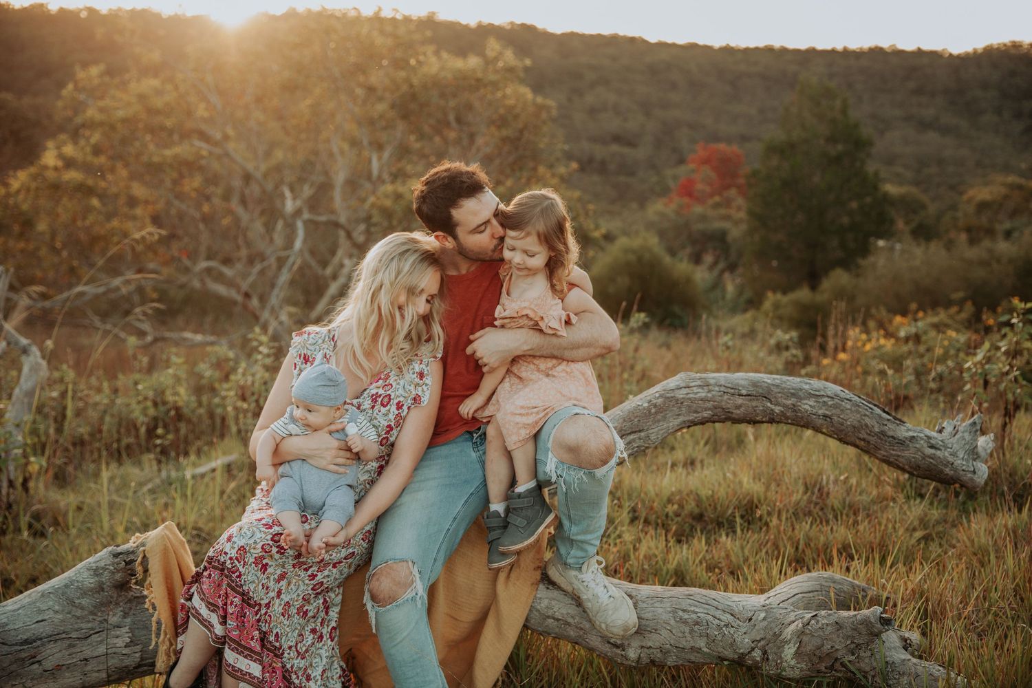 Family of four sharing tender moment on fallen log in autumn forest.