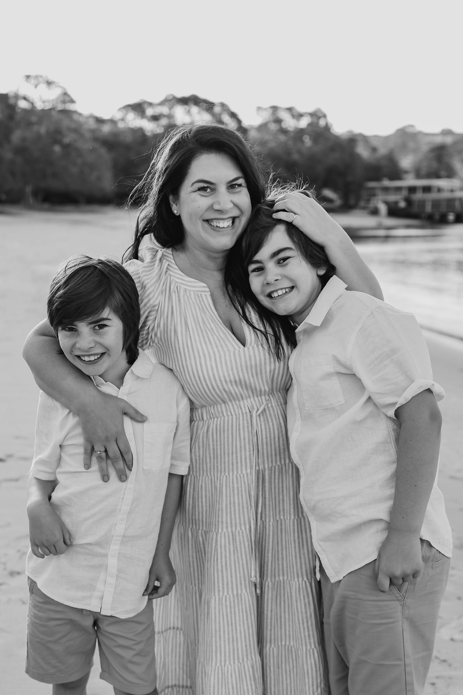 Black and white photo of smiling mother embracing two boys on beach.