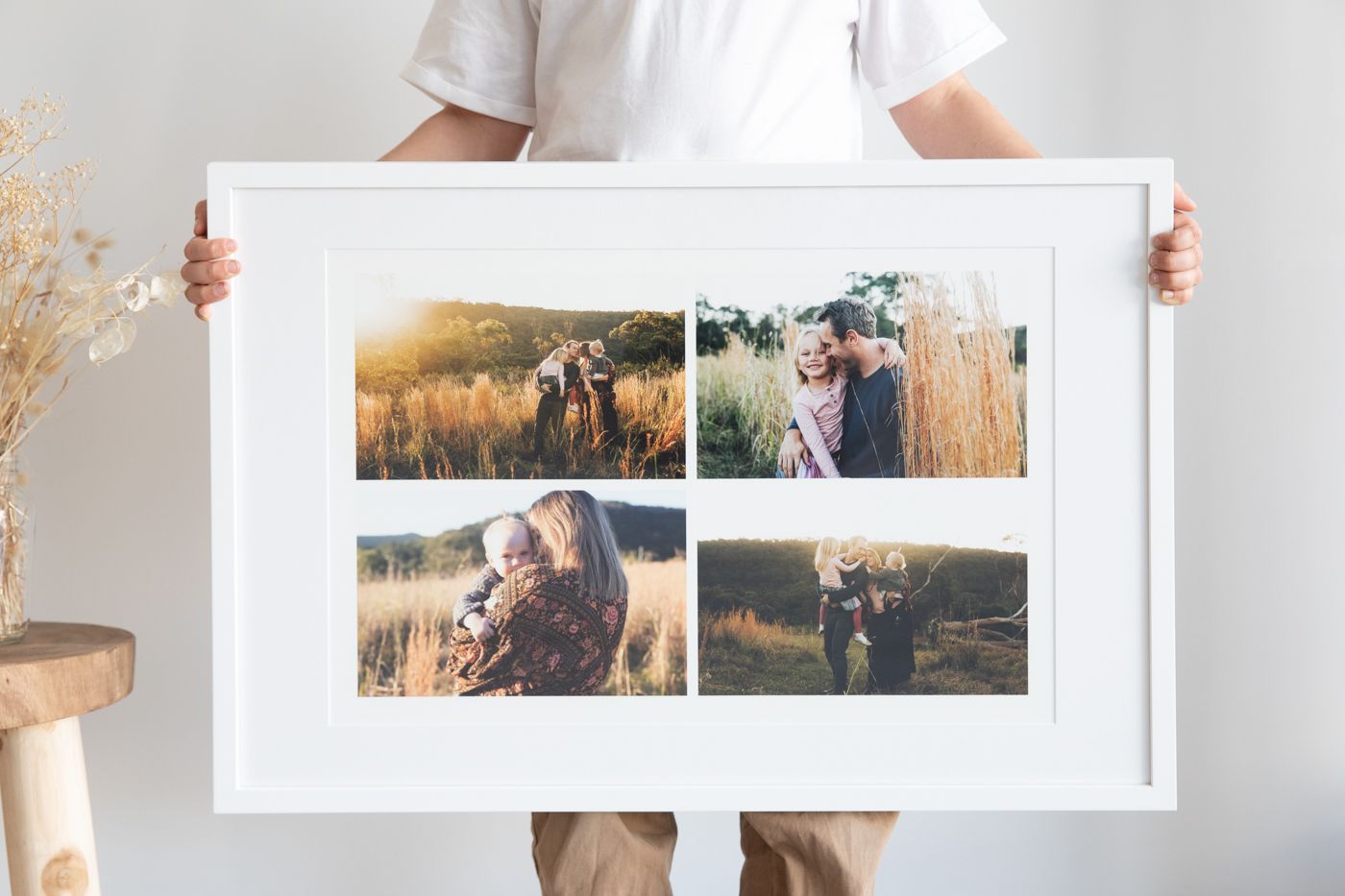 Person holding a large white framed photo collage print featuring four outdoor couple and family portrait photographs.