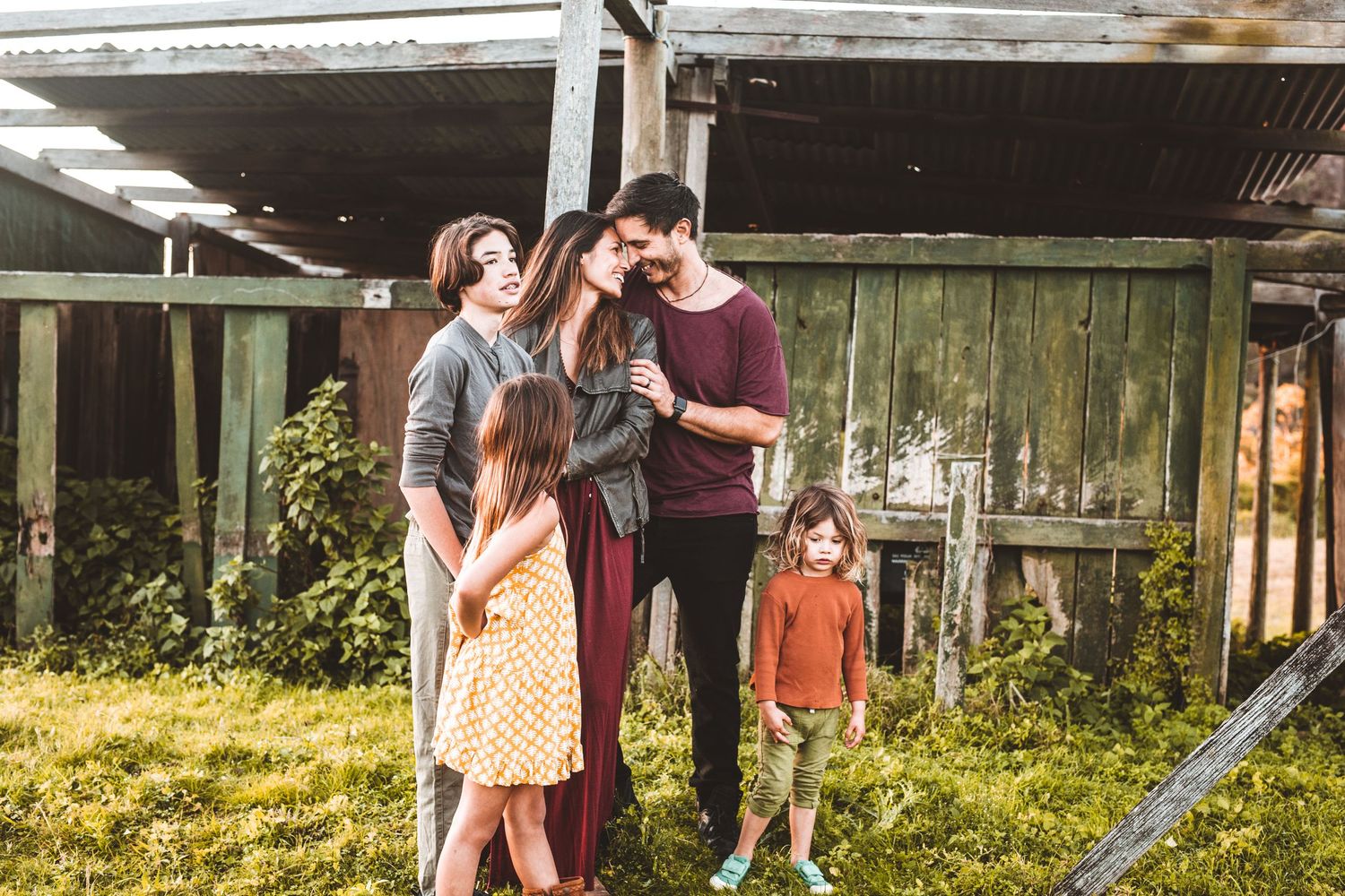 Family of five shares a warm embrace outdoors near a rustic wooden structure.