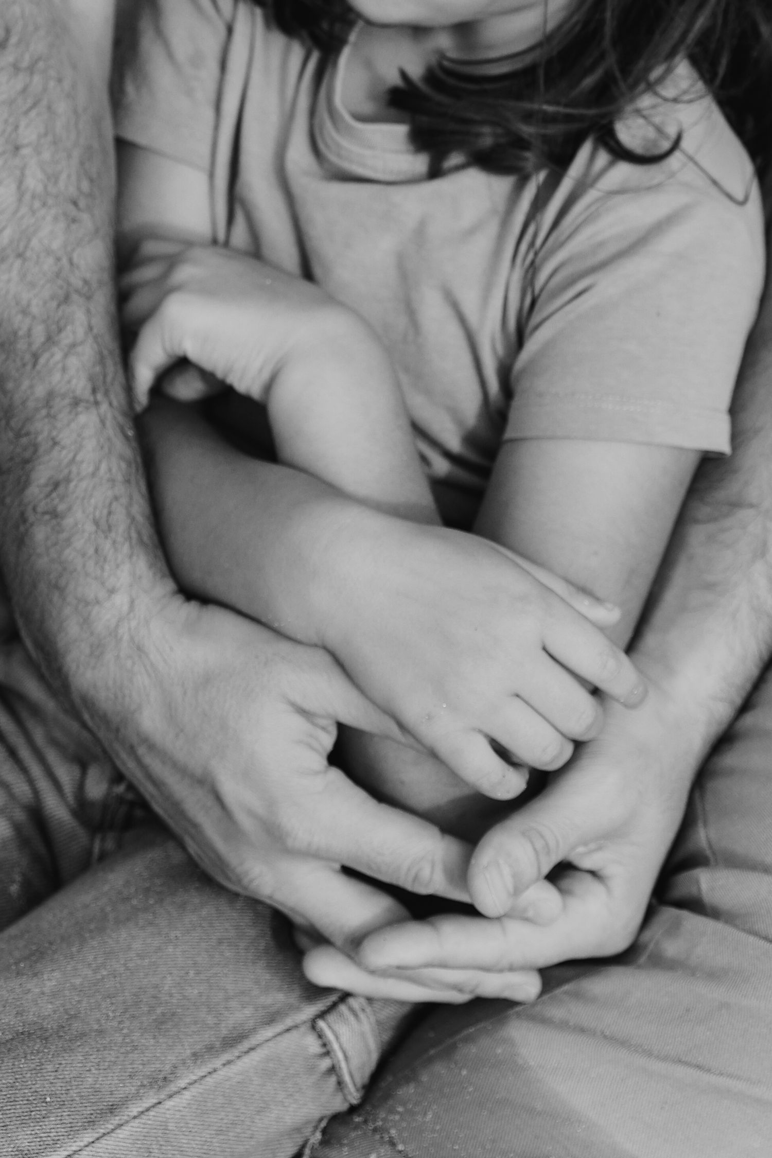 Black and white close-up of a father and child holding hands together in an intimate family moment.