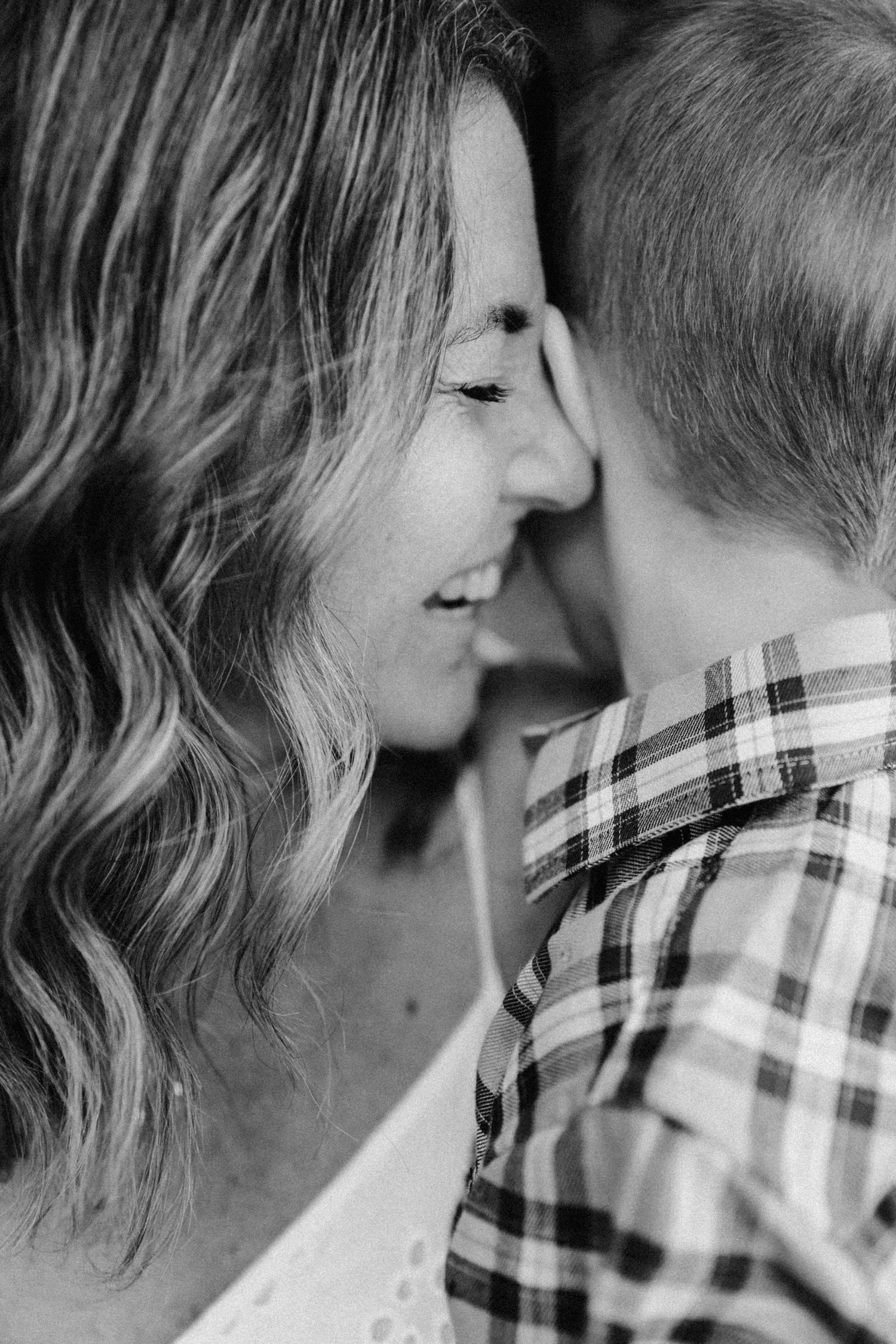 Black and white photo of a smiling woman tenderly touching foreheads with a young boy in a plaid shirt.