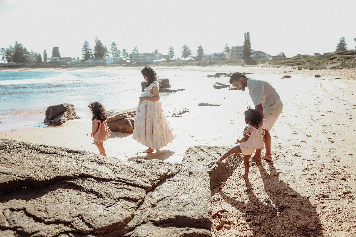 Family with two young children exploring rocky beach shoreline on a sunny day.