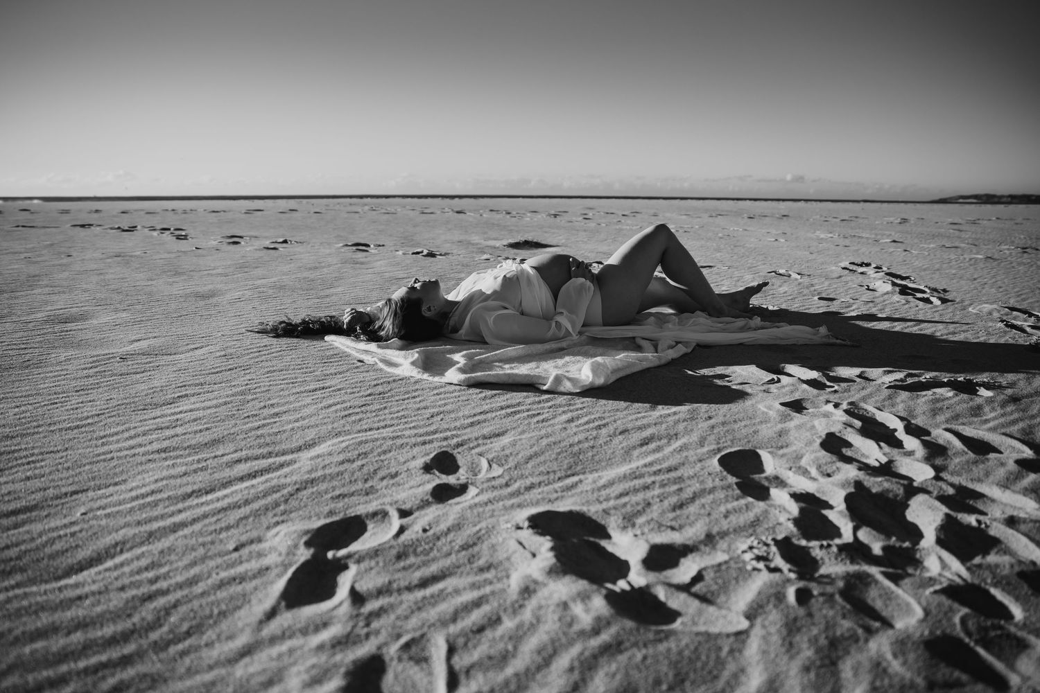 Black and white photo of a person lying on a blanket in a vast sandy desert landscape.