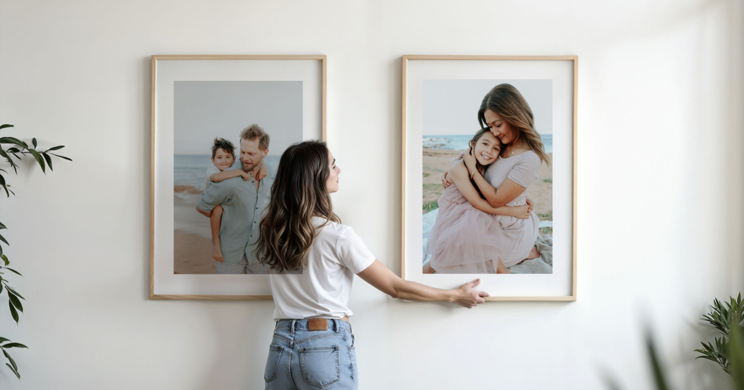 Woman hanging two large framed family beach photos on a white wall next to a green plant.