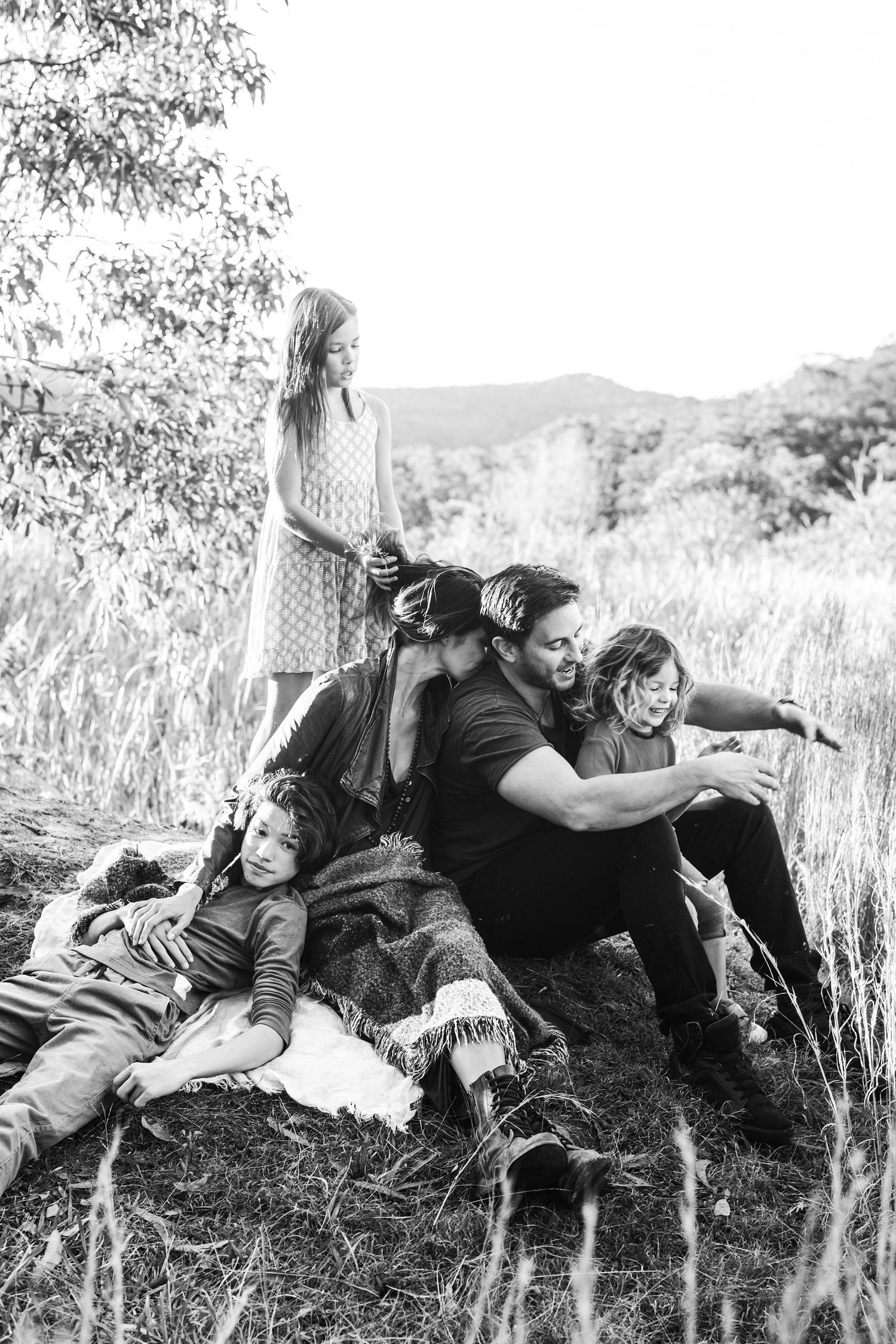 Black and white family photo of parents and children playing together in a grassy field surrounded by trees.
