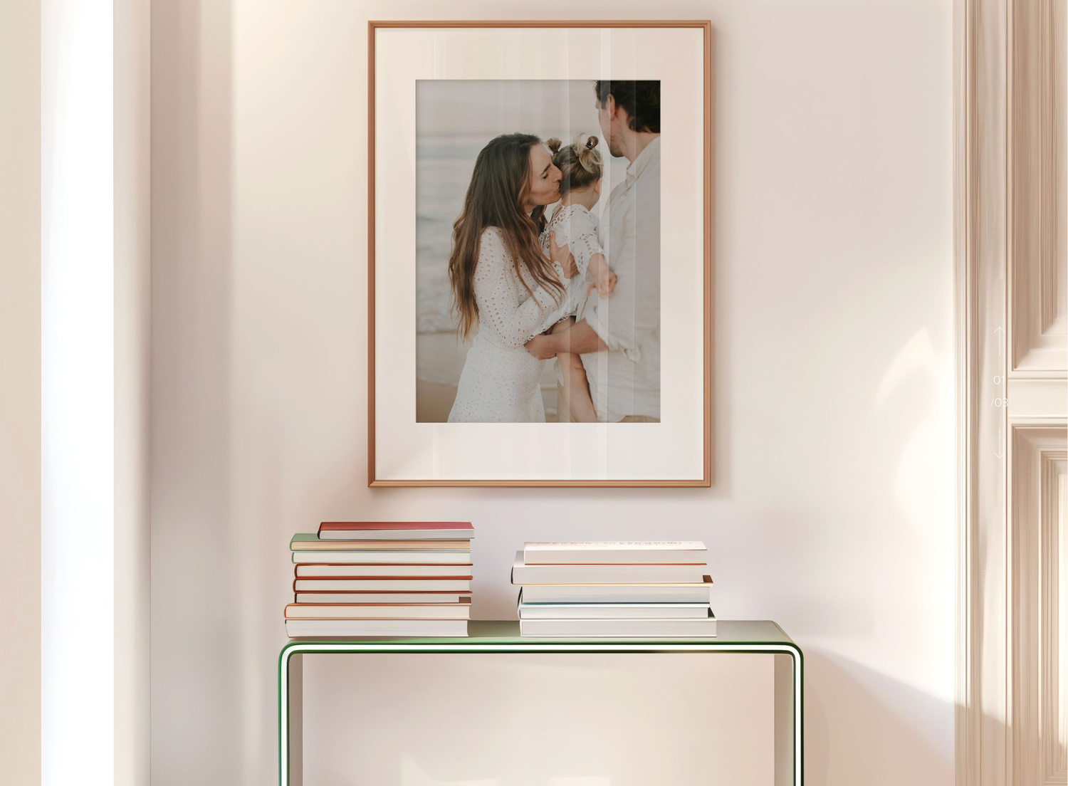 Framed family portrait in wooden frame hanging on wall above glass console table with stacked books.