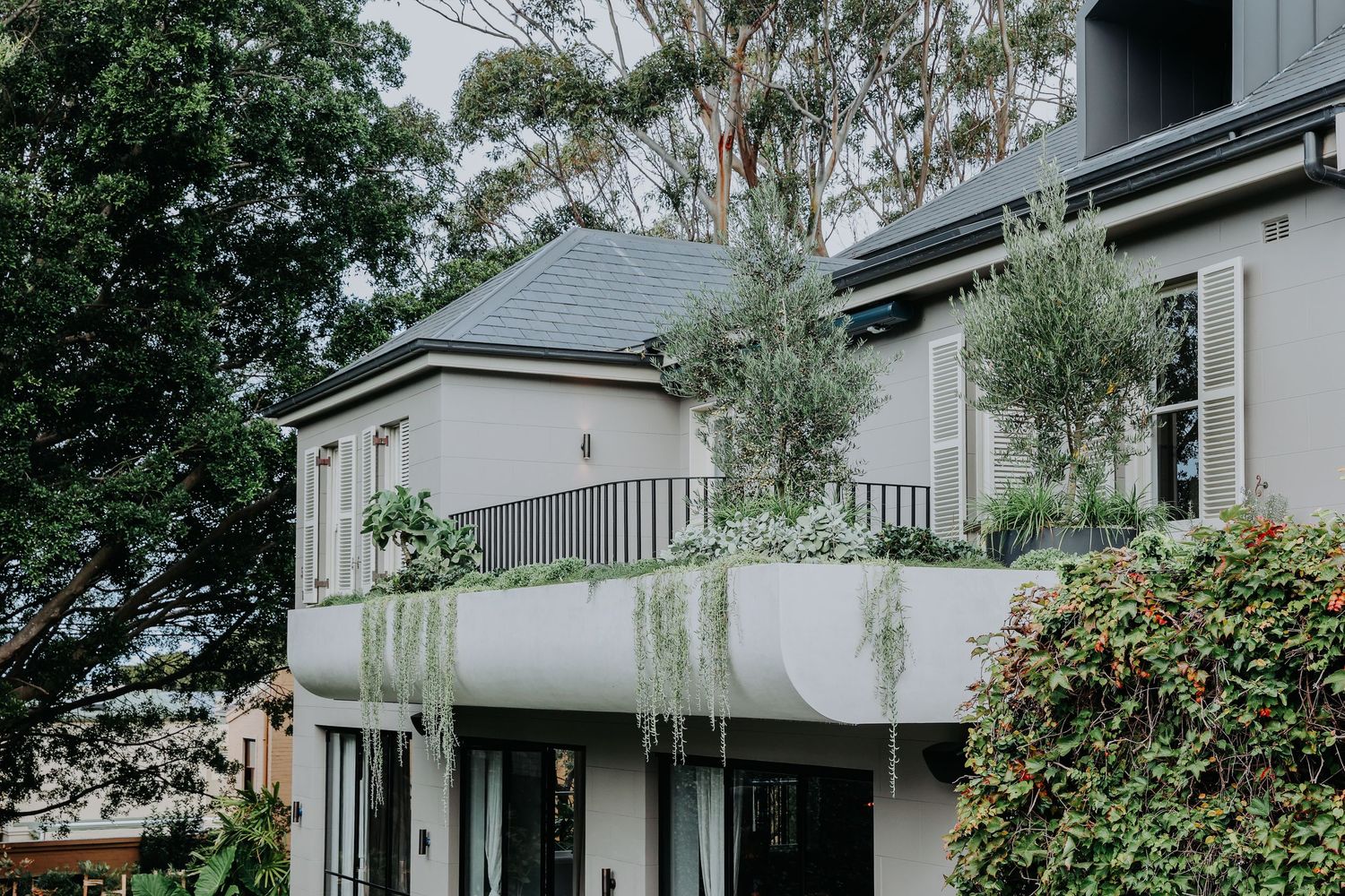 Elegant two-story home exterior with lush greenery, balcony plants, and cascading vines.