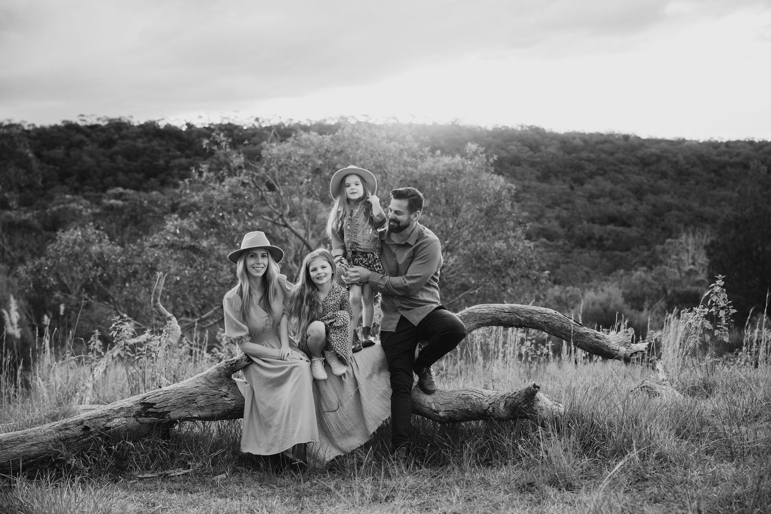 Family of four posing on fallen log in scenic countryside, black and white photo.