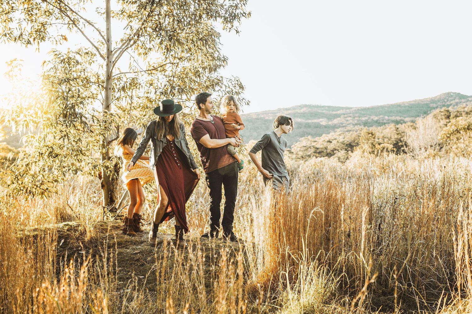 Family walking through golden sunlit meadow with rolling hills in background on a warm sunny day.