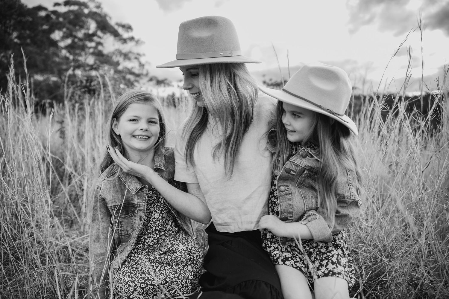 Black and white photo of a mother and two daughters laughing together in a field of tall grass.