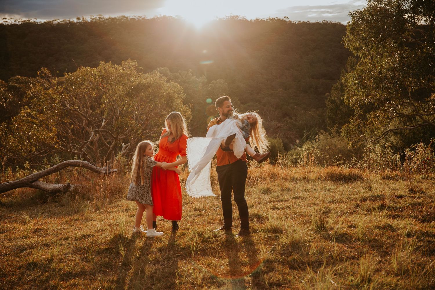 Family of four enjoying a golden sunset in a scenic outdoor meadow setting.