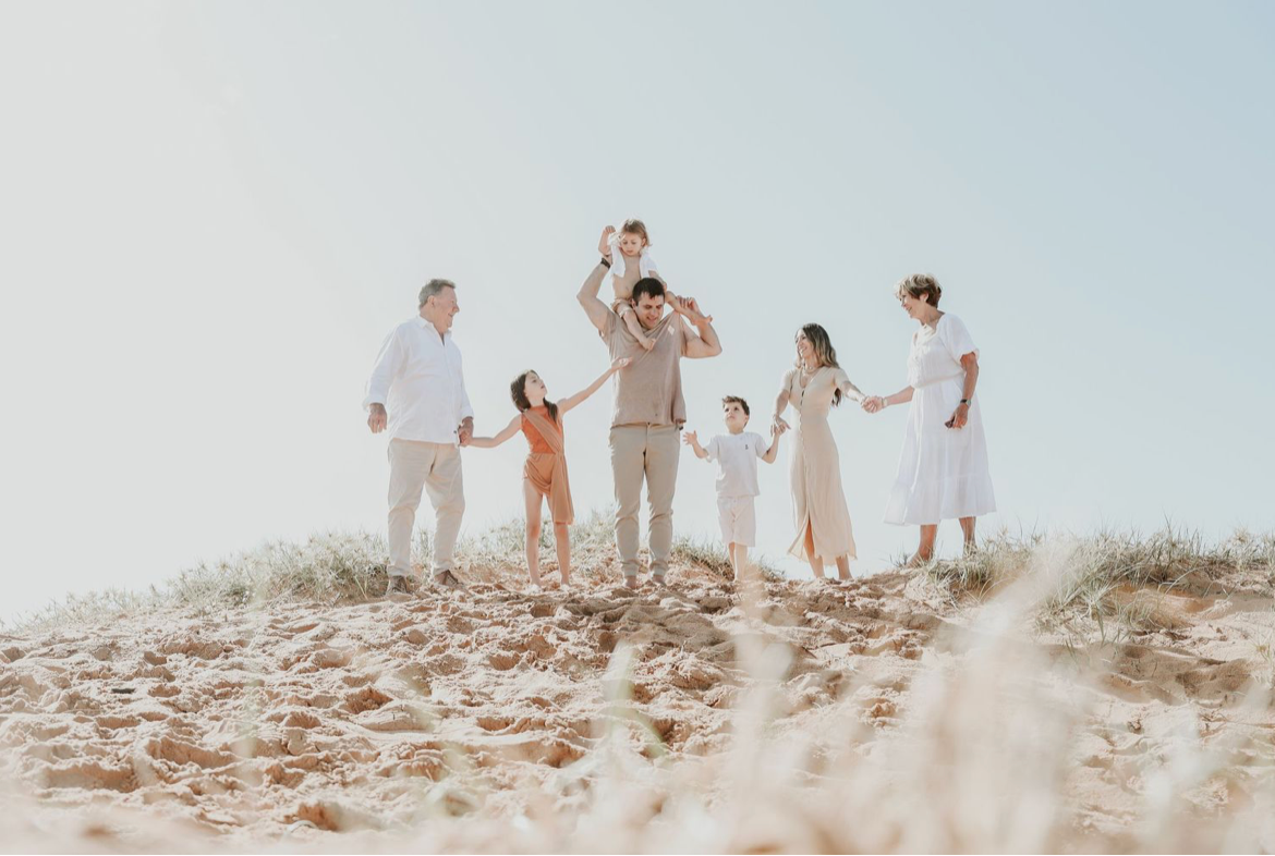 Extended family group photo on a sunny sand dune, dressed in white and neutral tones.