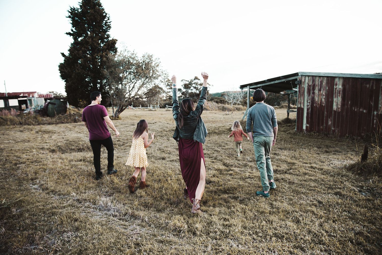 Family of five playing and walking together in a rustic farm field at dusk.