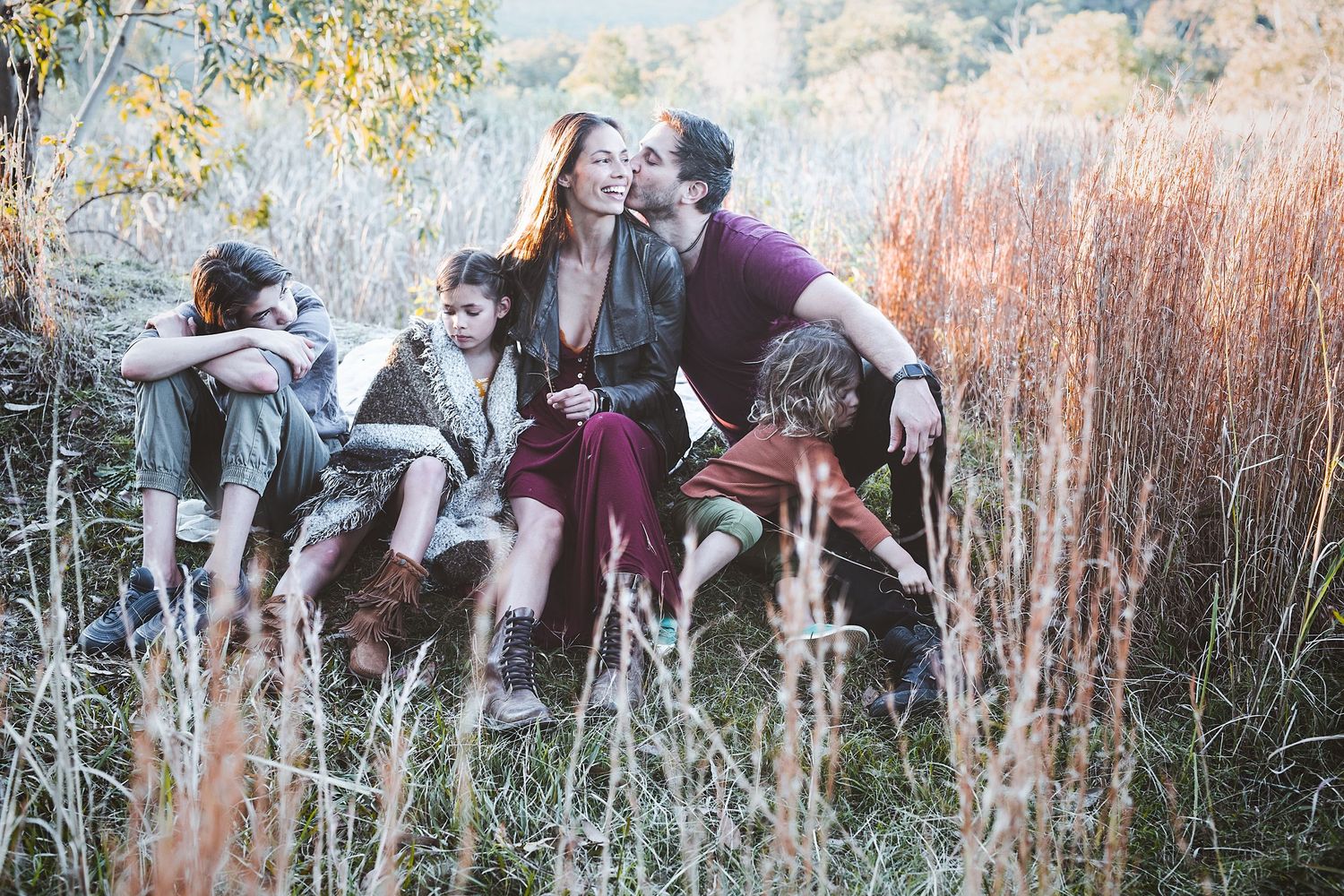Happy family sitting together in golden autumn fields, candid outdoor portrait.
