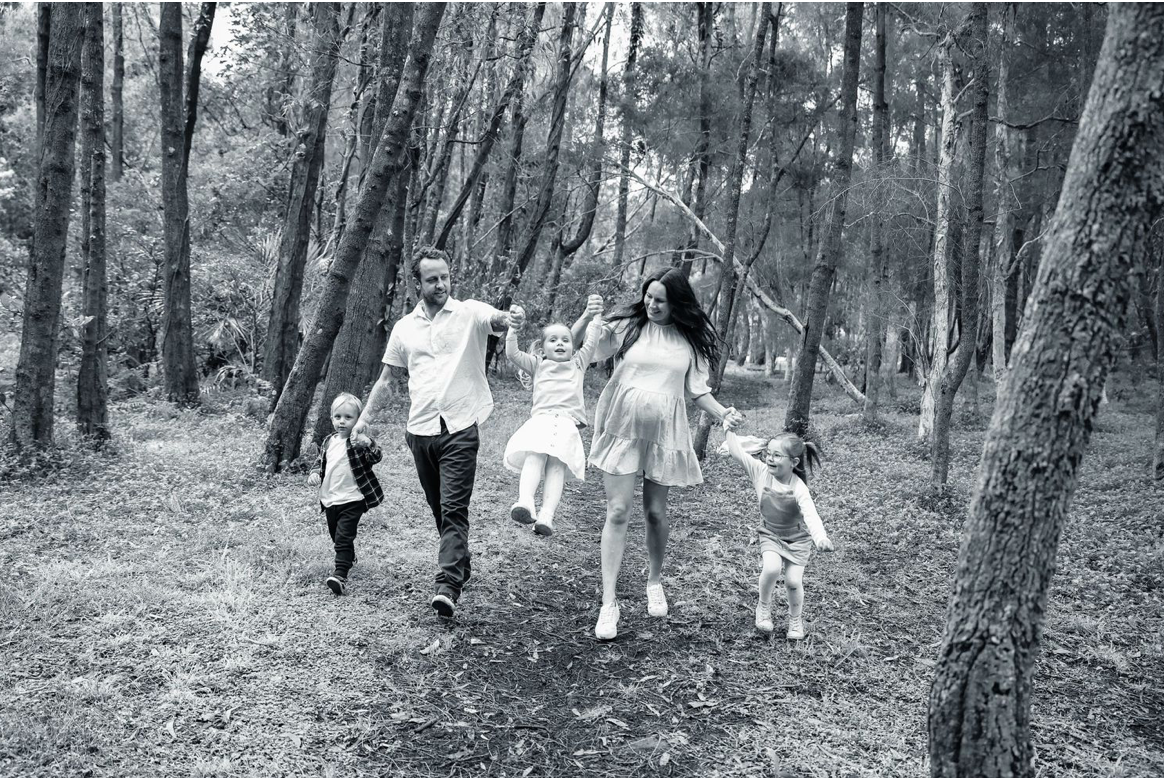 A happy family with three children walks playfully through a forest in black and white photo.